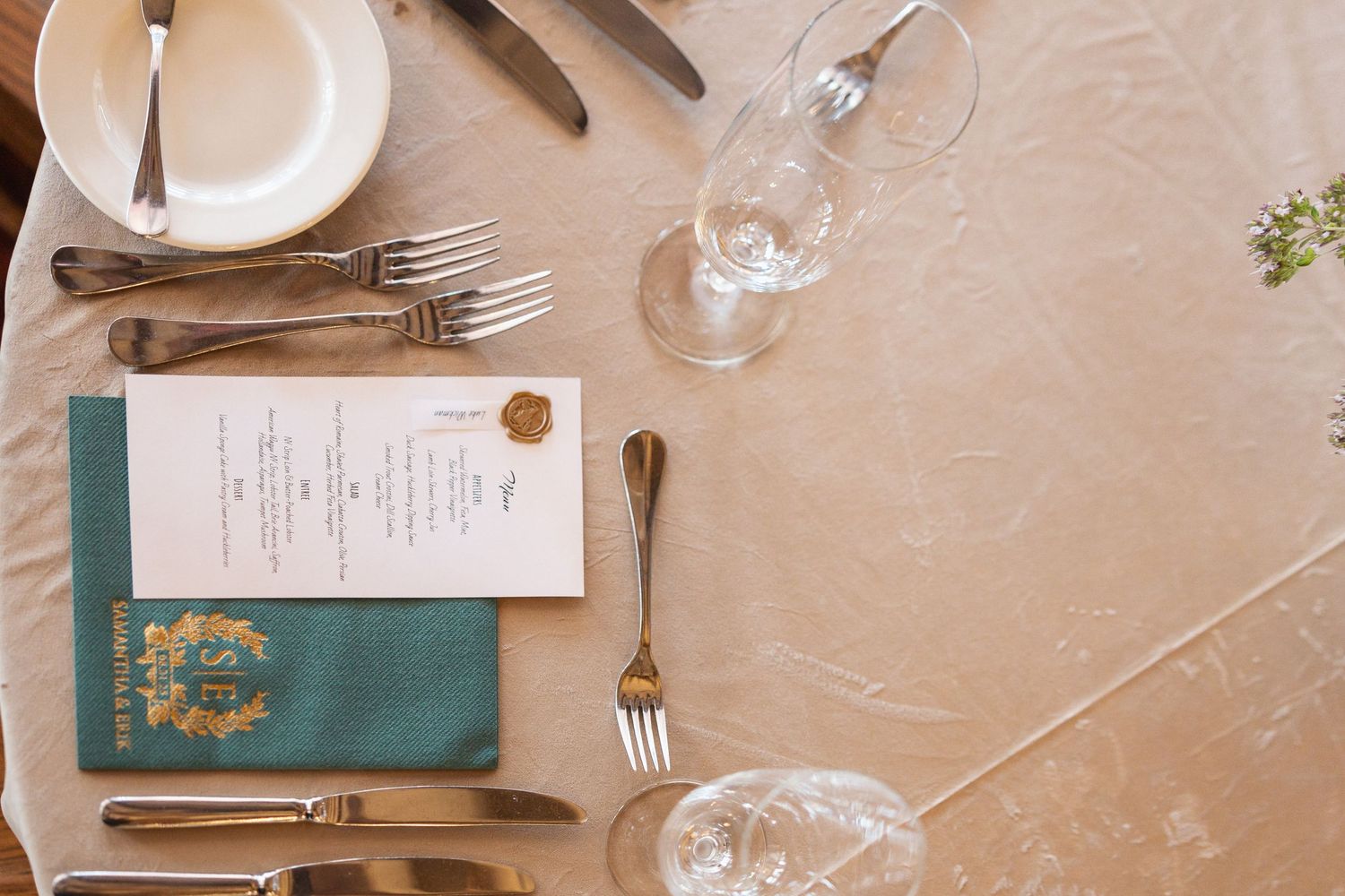 Elegant place settings with teal menus and gold flatware arranged on a neutral beige tablecloth.