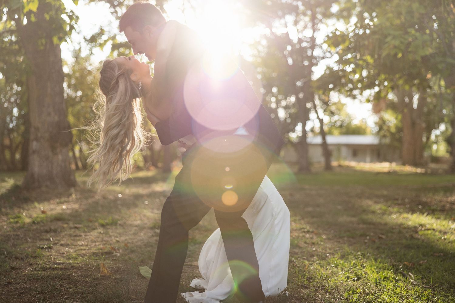 Golden sunlight streams through trees as a couple shares a romantic moment.