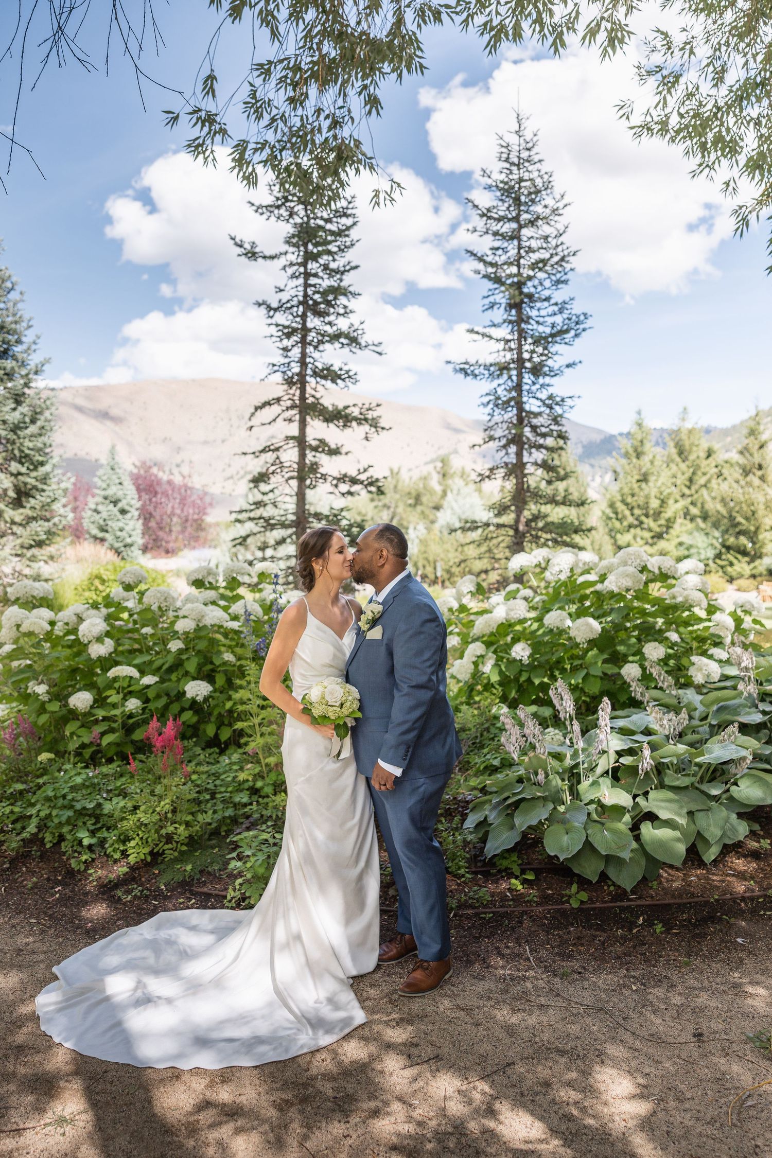 Wedding couple poses in garden with mountain backdrop and blooming hydrangeas.