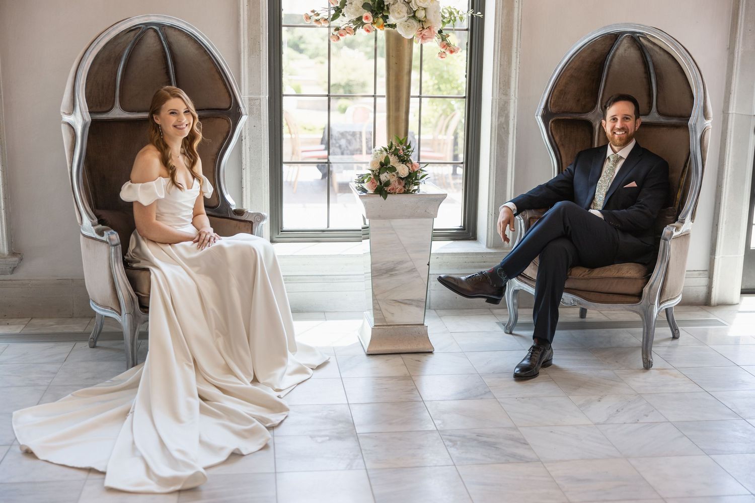 Wedding couple shares intimate moments in an elegant room with vintage chairs and large windows.