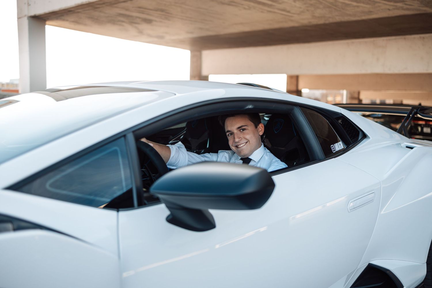 White luxury sports car parked in a concrete parking structure with natural lighting.