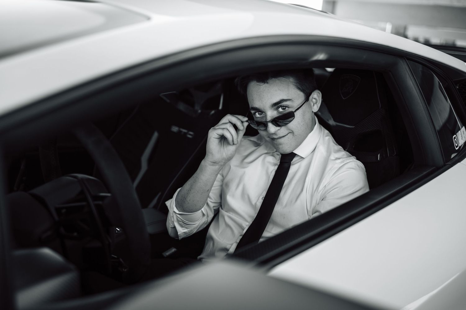 Driver in formal attire seated in luxury vehicle interior during evening hours.