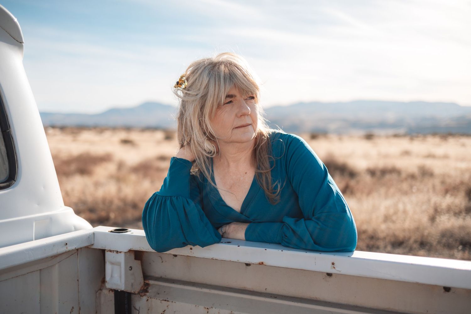 Person in blue shirt gazing at desert landscape through car window on sunny day.