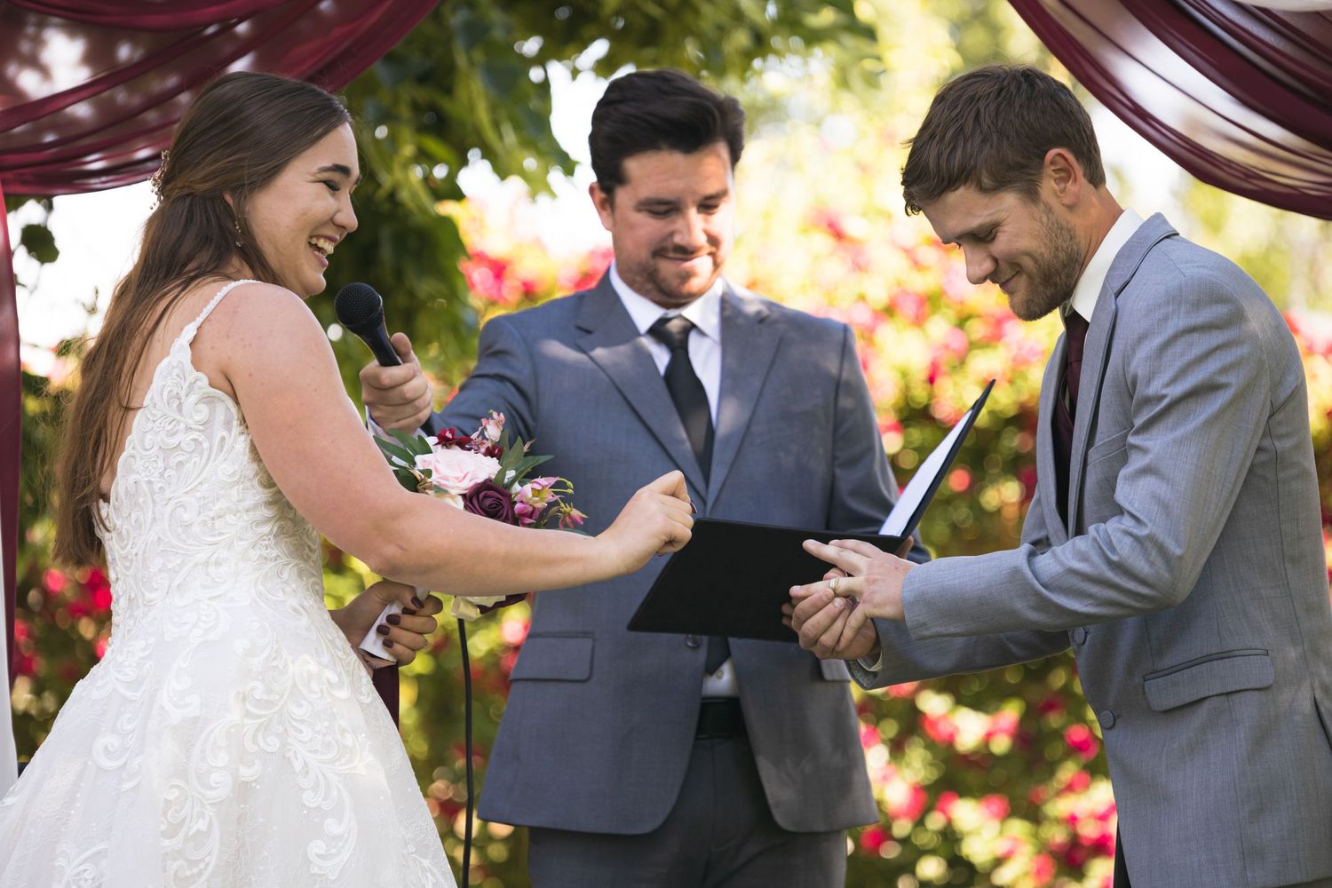 An intimate outdoor wedding ceremony moment under burgundy drapery.