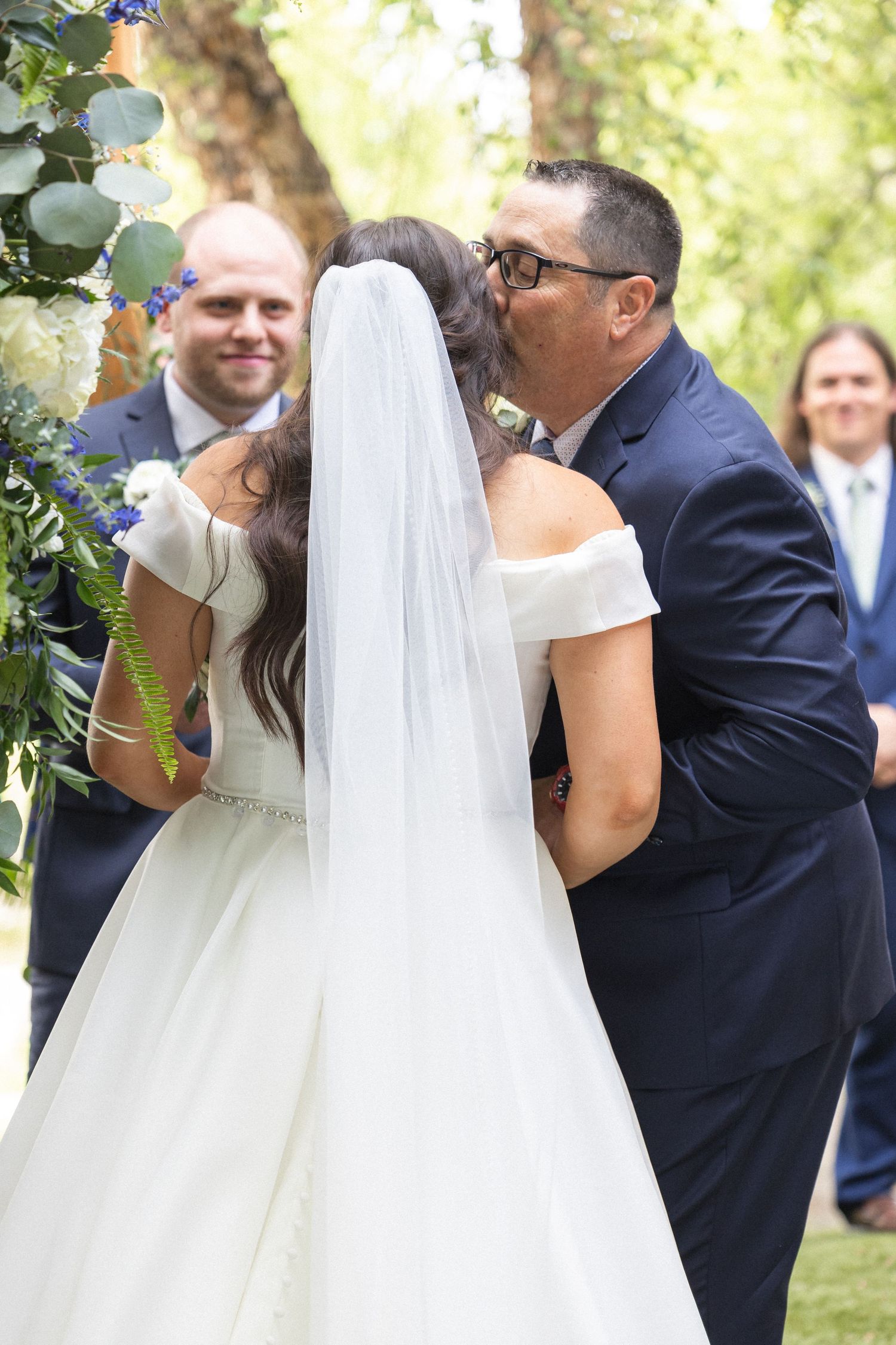 A tender moment captured during an outdoor wedding ceremony under floral decorations.