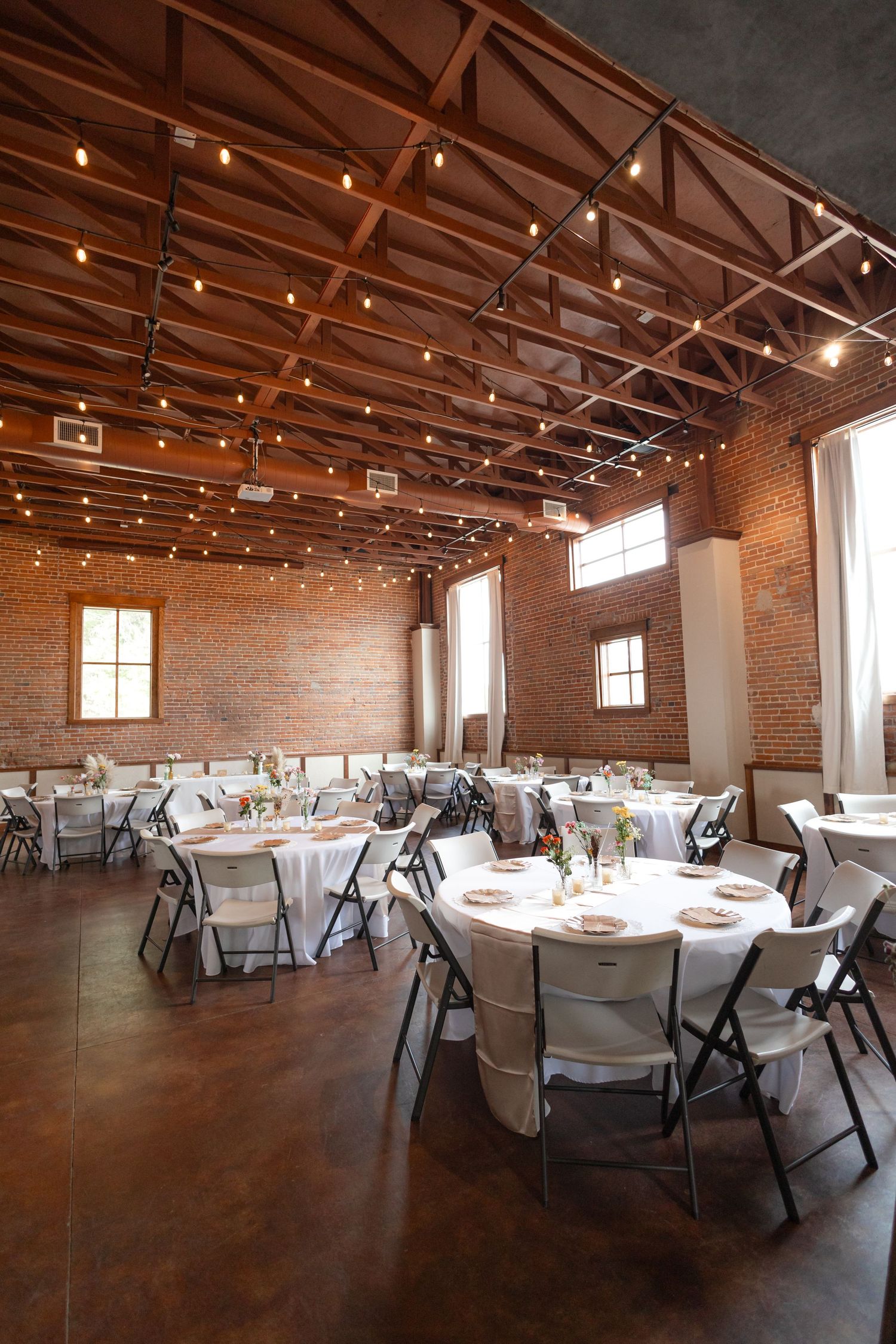 Industrial reception venue with exposed brick walls, string lights, and round tables.