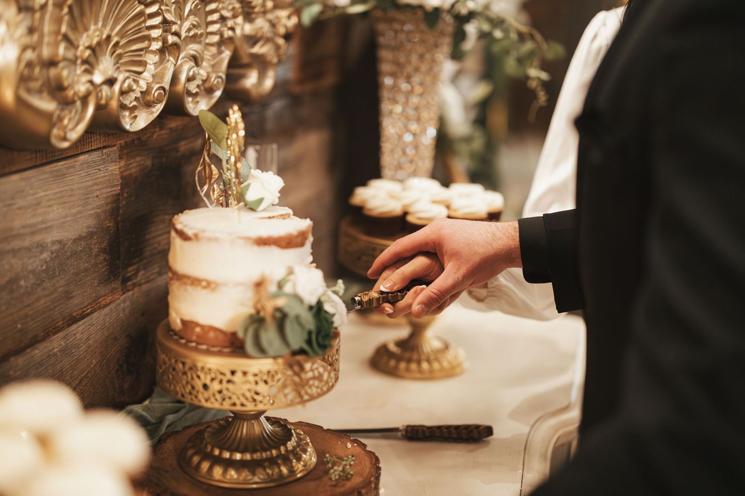 Elegant wedding cake being served on ornate gold stands with rustic wooden backdrop.