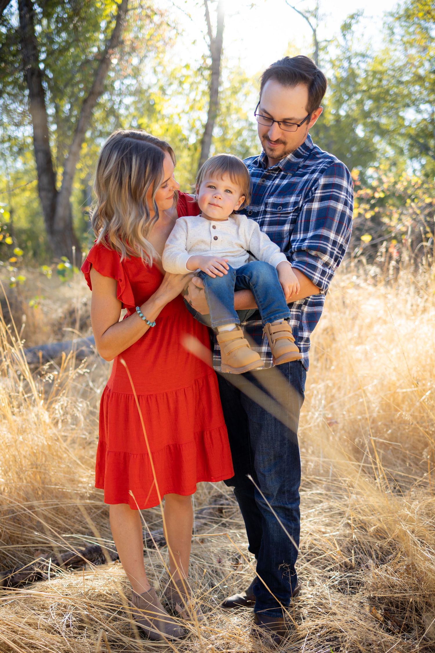 A family in coordinated red and blue outfits poses together in a sunlit field of golden grass during autumn.