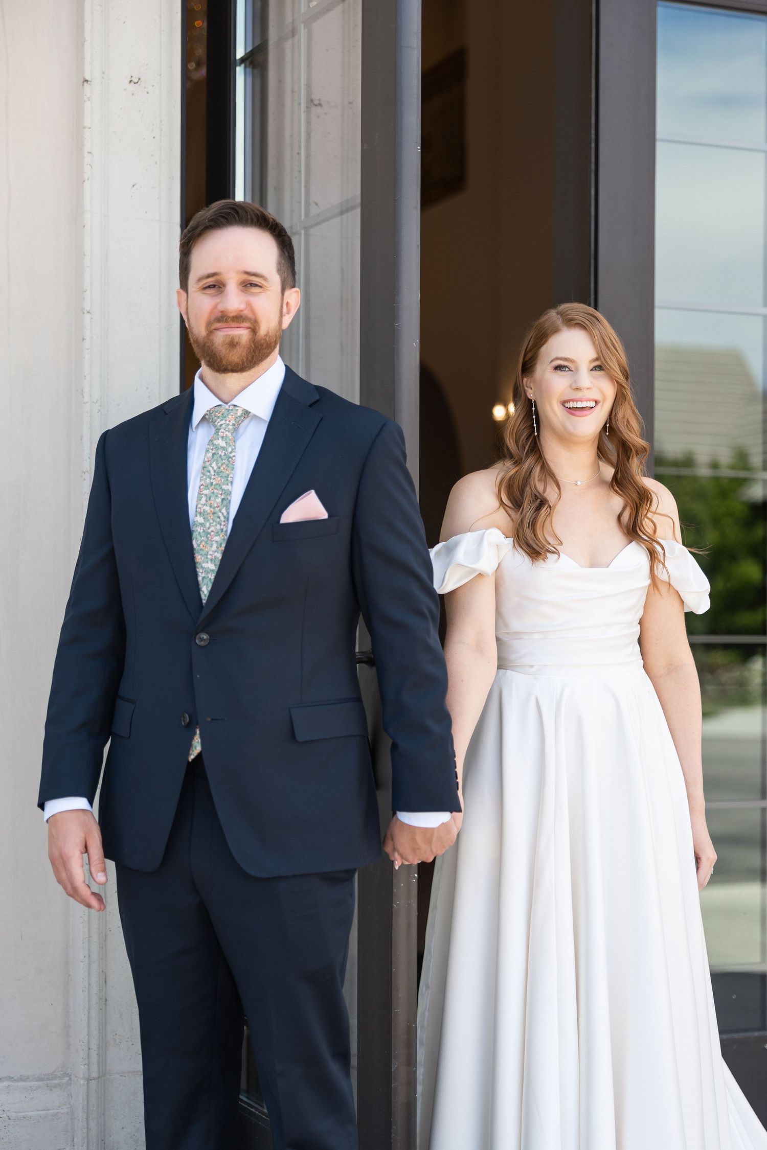 Couple shares a joyful moment during their first look photo session outside a white building.