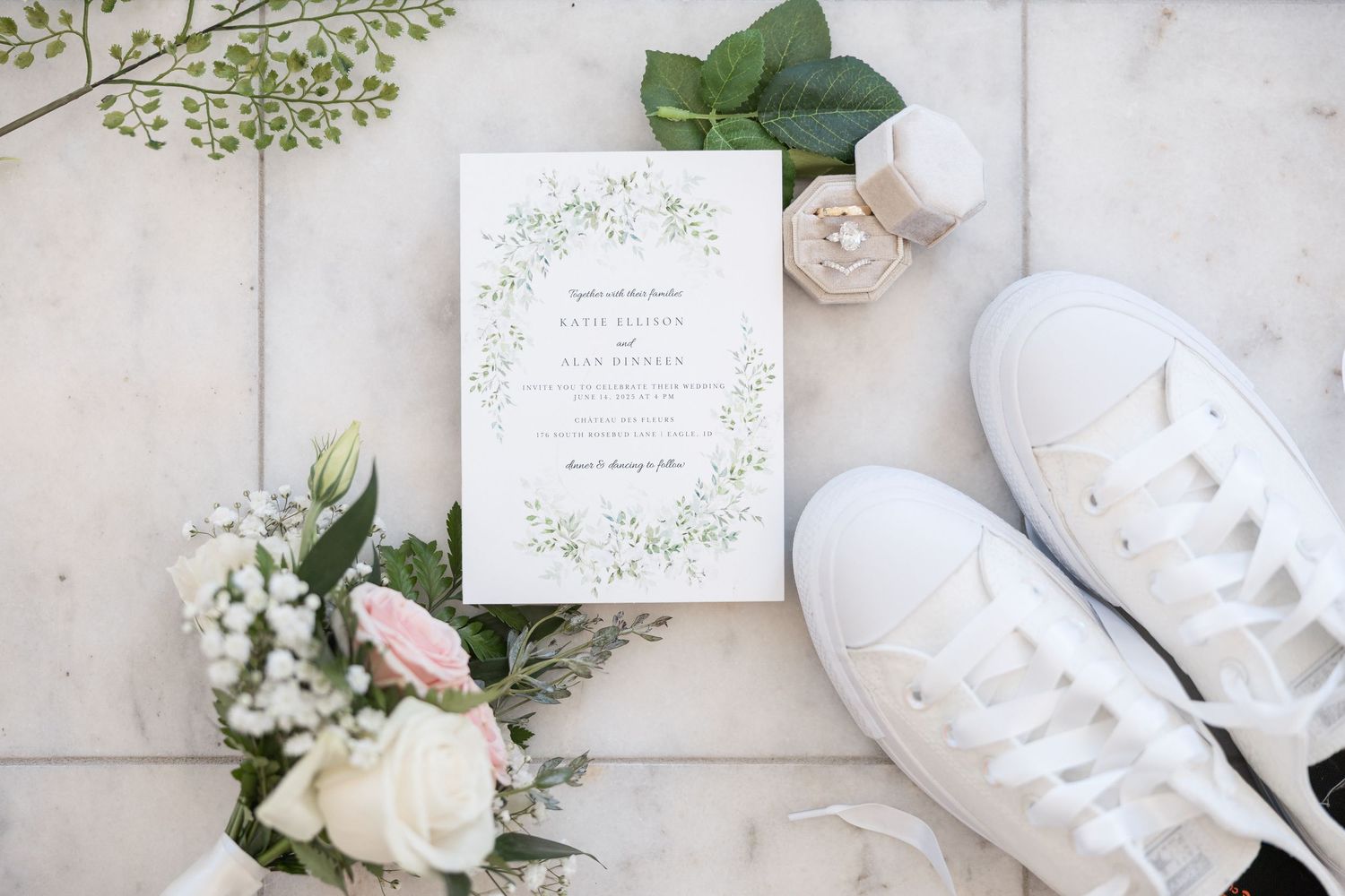Wedding invitation suite with floral design laid out on marble surface with white sneakers and roses.