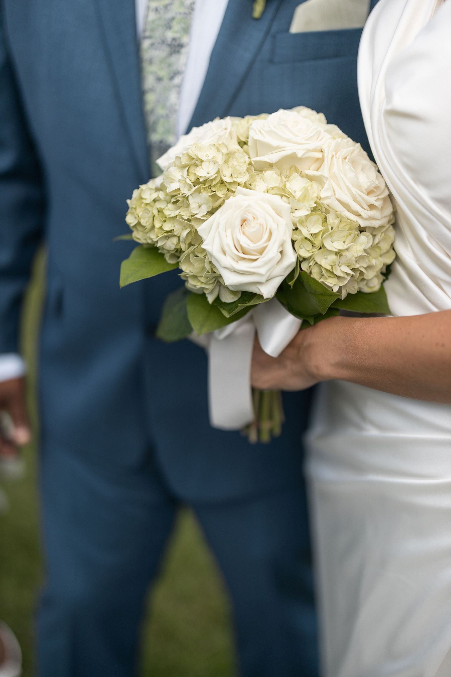 White roses and hydrangea bouquet details against navy blue suit and white dress.