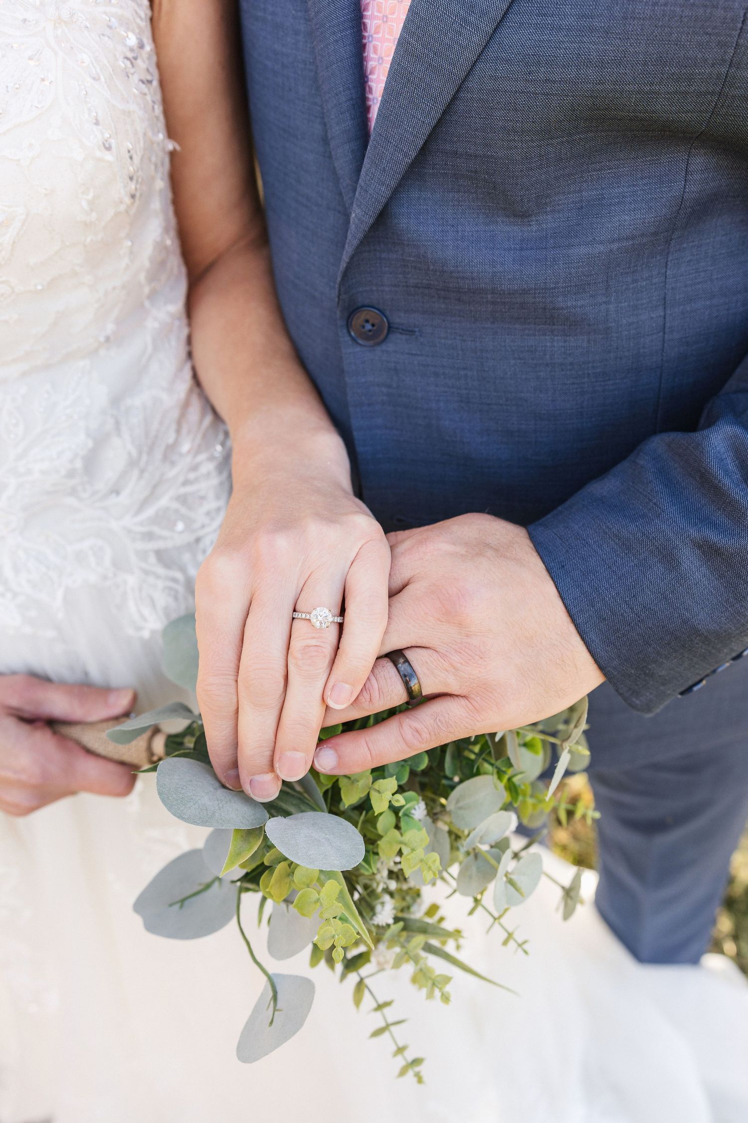 Close-up of wedding rings and hands holding a eucalyptus bouquet.