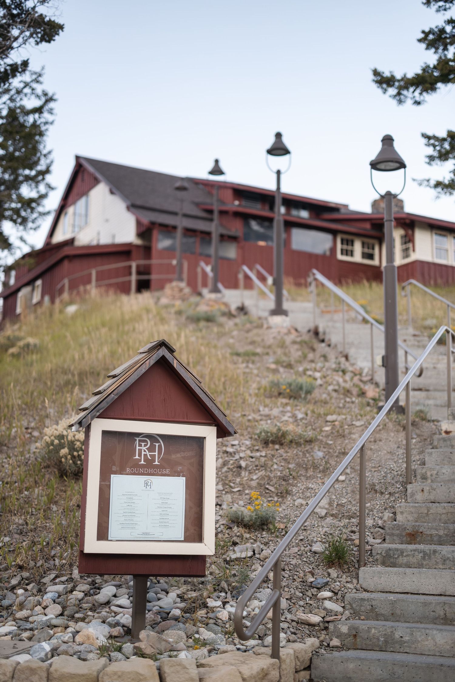 Rustic wooden signs line a rocky hillside path leading to red buildings.