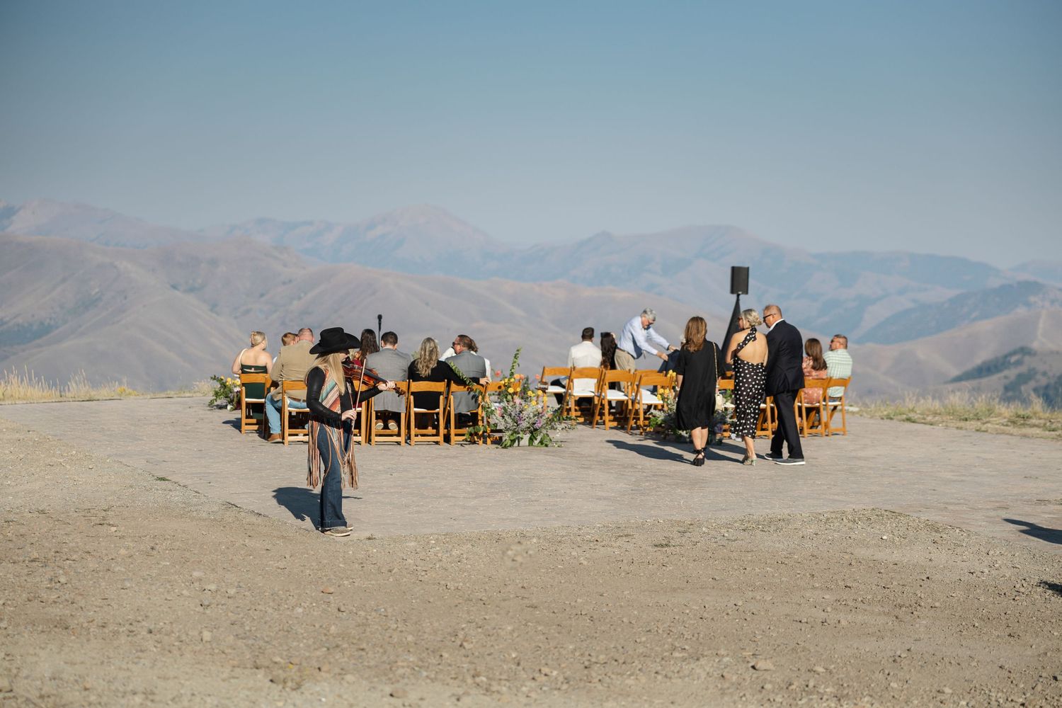 A panoramic view of people dining at tables in the desert with mountains in the background during sunset.