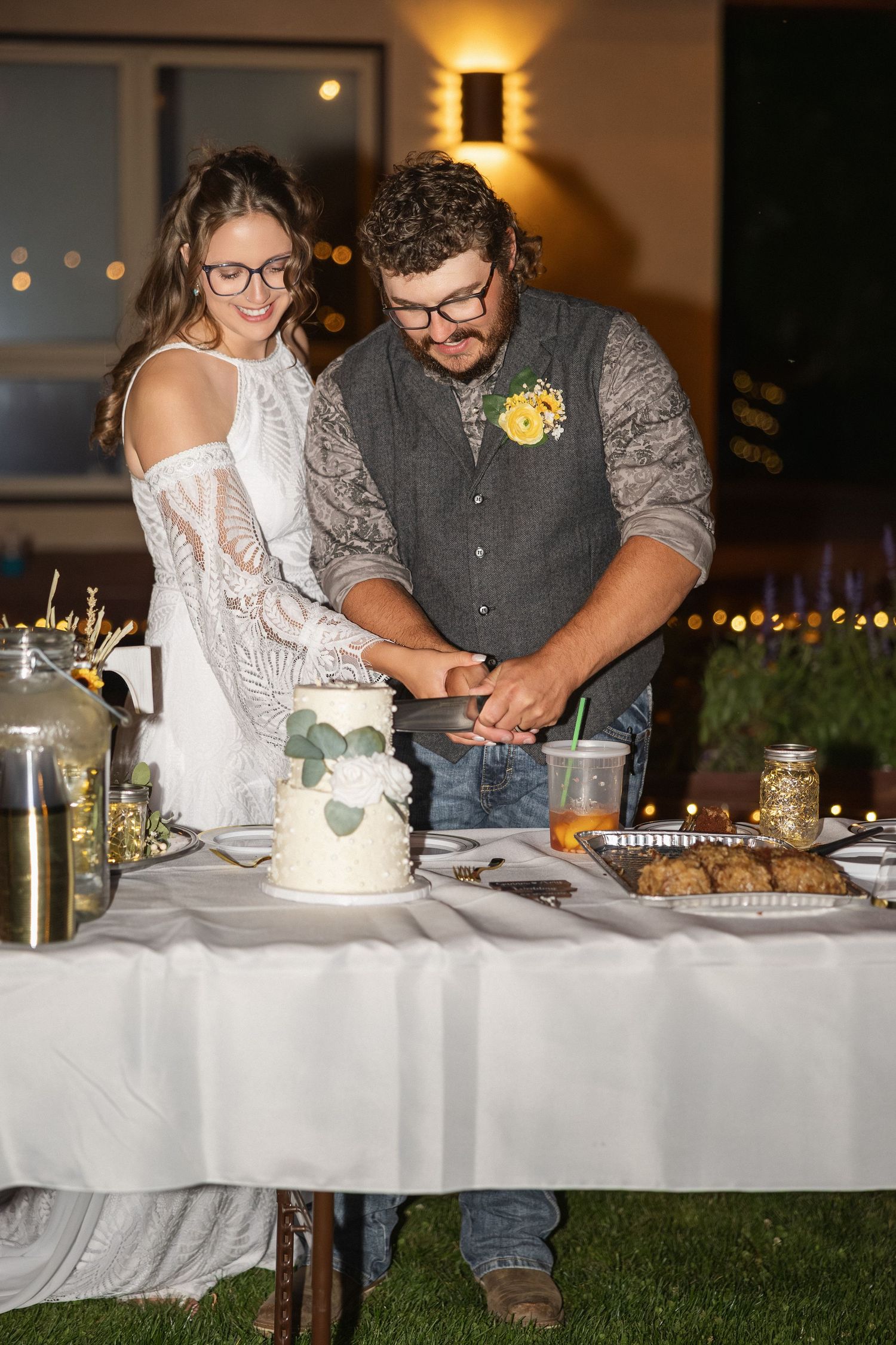 Wedding dessert table setup with white cake and cookies illuminated by warm ambient lighting.