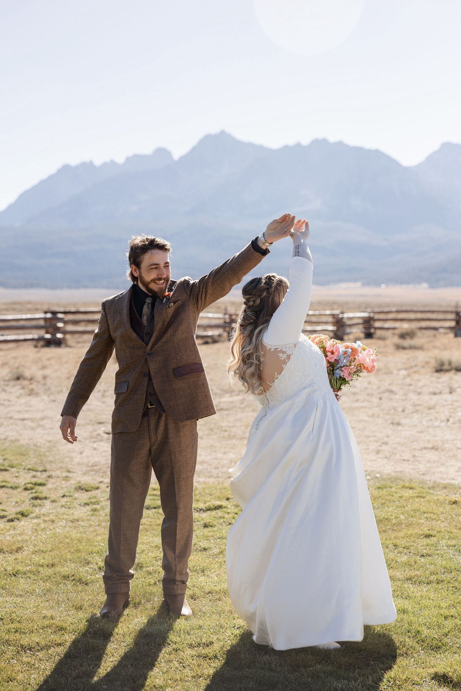 A couple in wedding attire dances playfully in a desert landscape with mountains in the background.