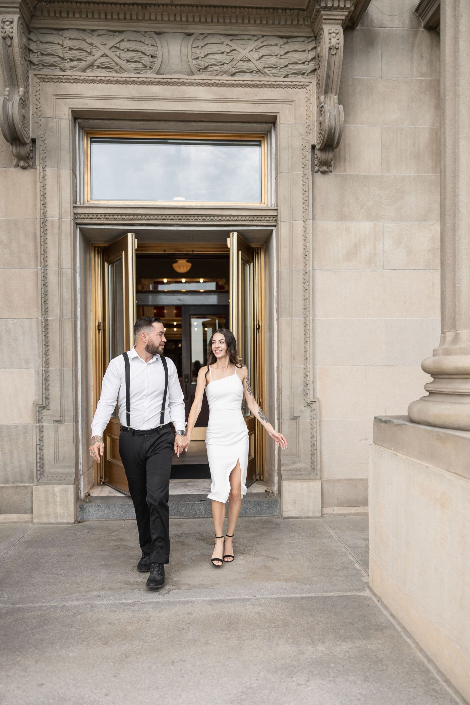 Couple in formal attire poses together in an elegant stone archway during a photoshoot.