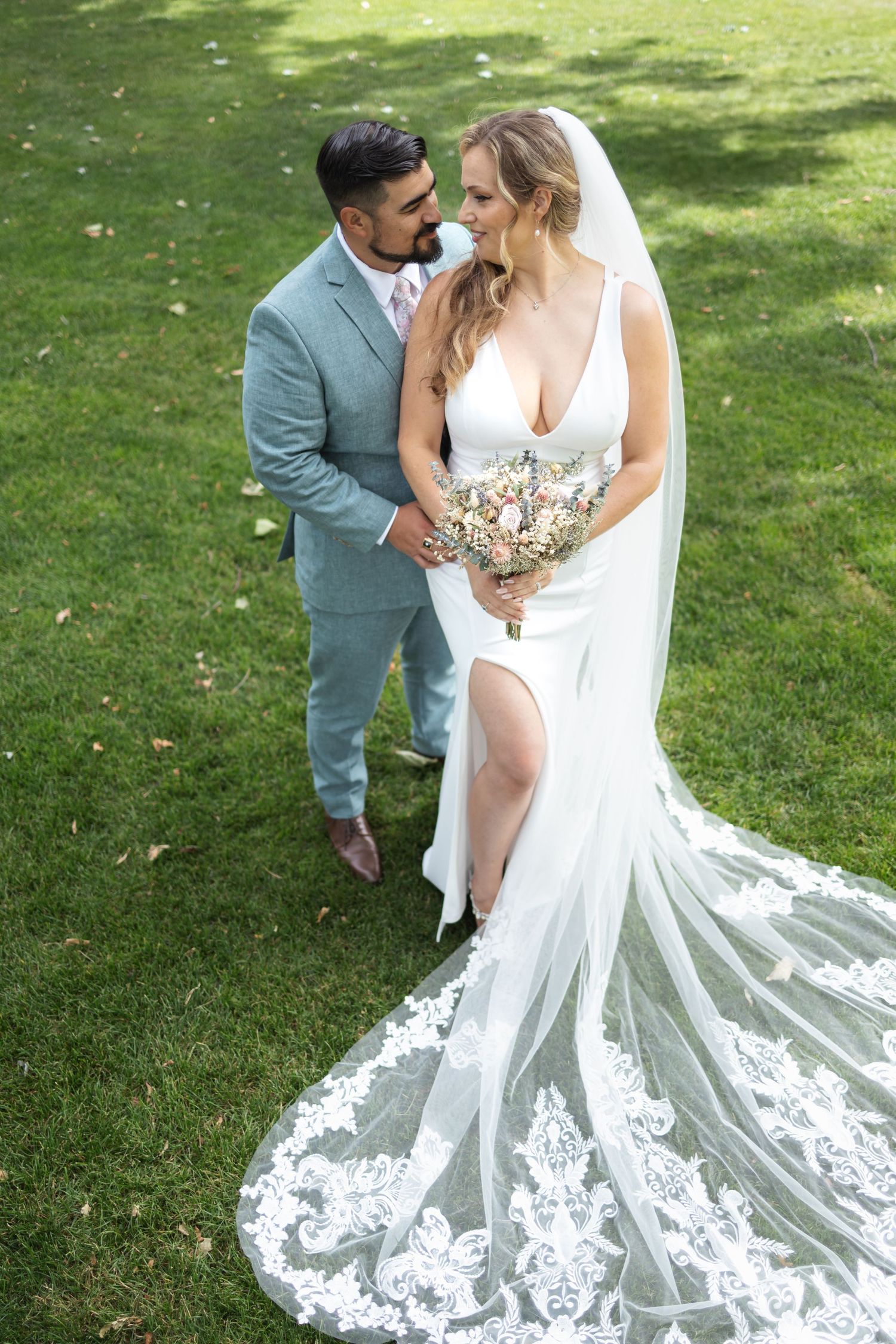 Intimate wedding portrait of couple in elegant white dress and blue suit on grassy lawn.