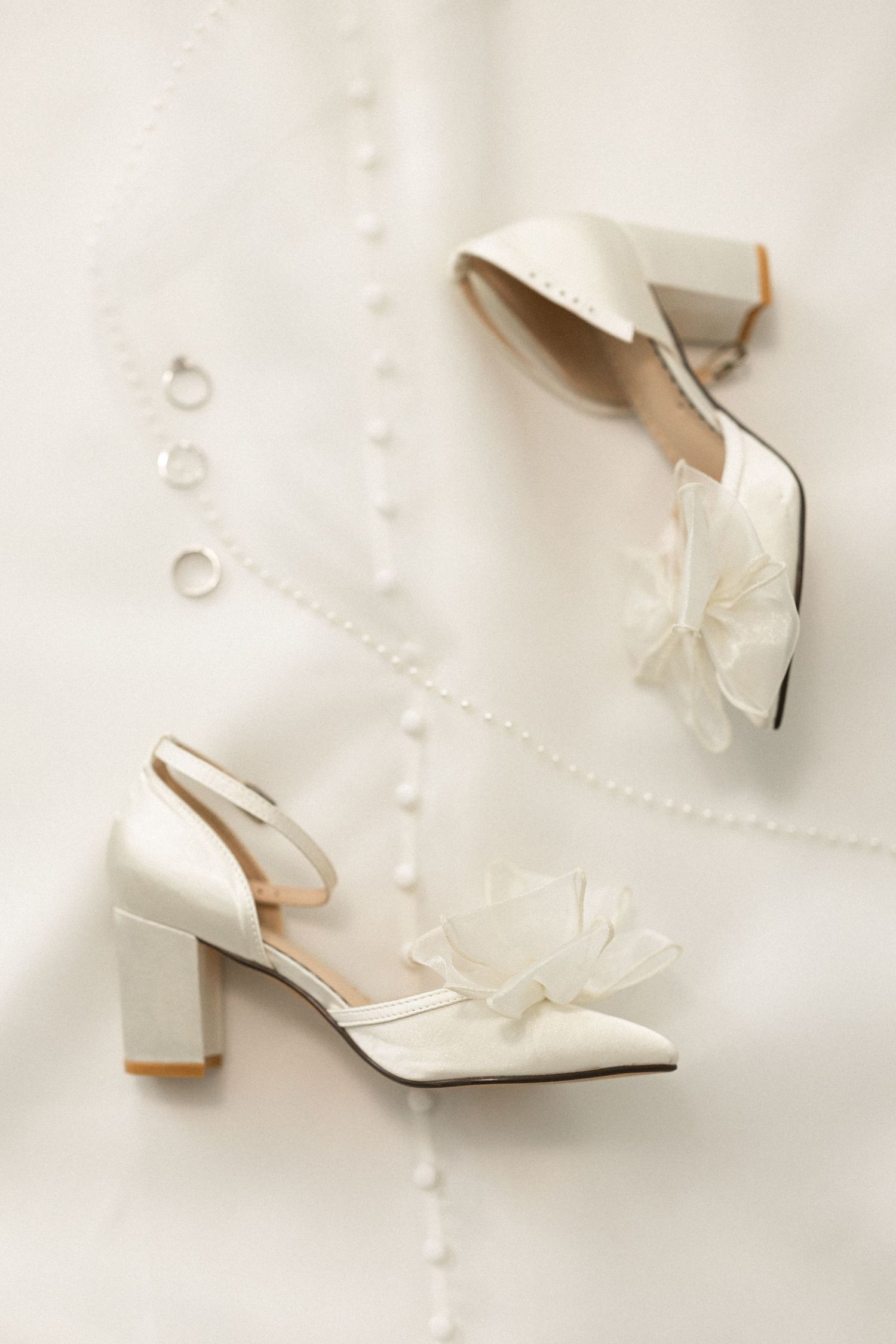 Elegant white bridal shoes with bow detail and block heel on light background.