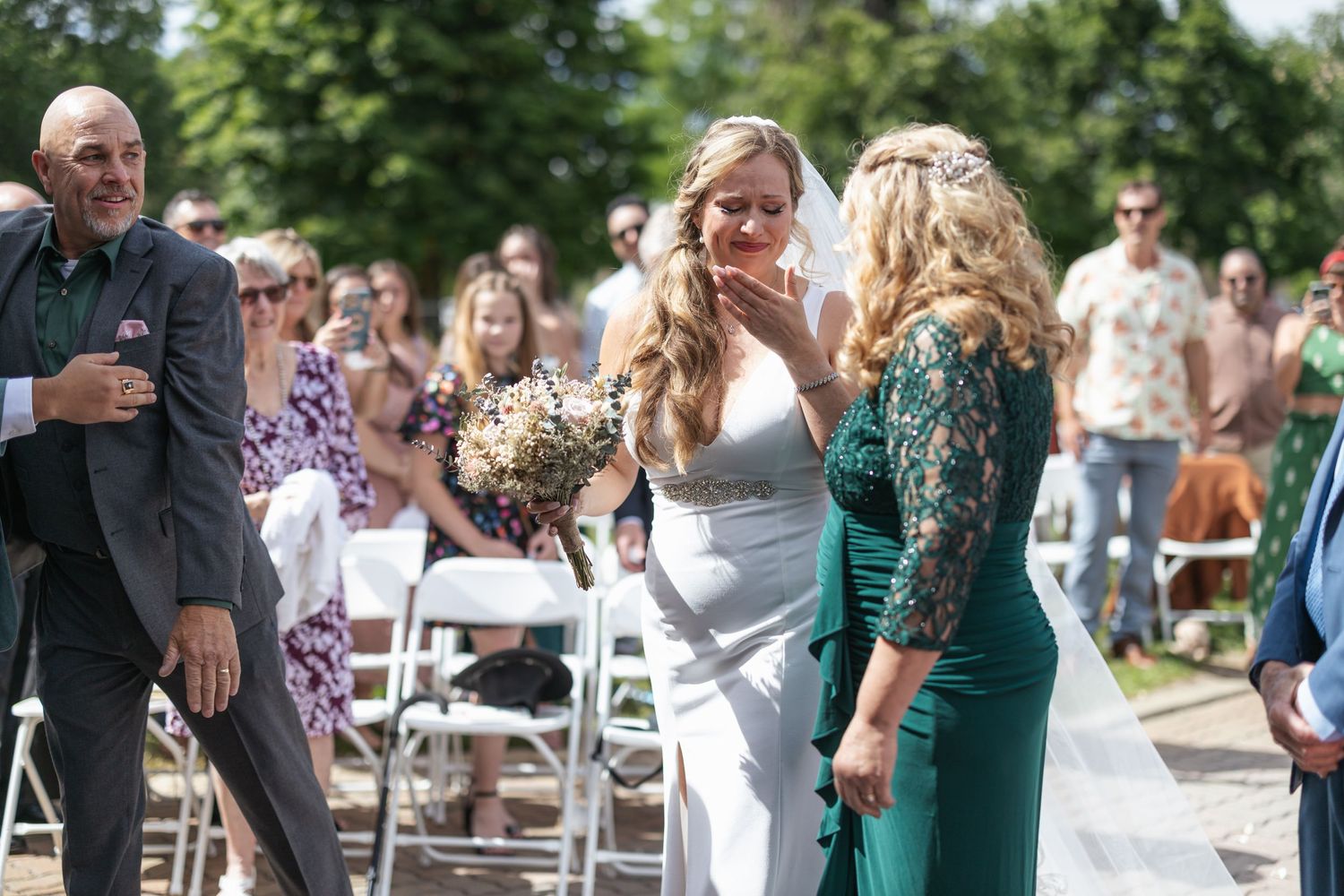Wedding guests socialize during an outdoor reception with white chairs and greenery.