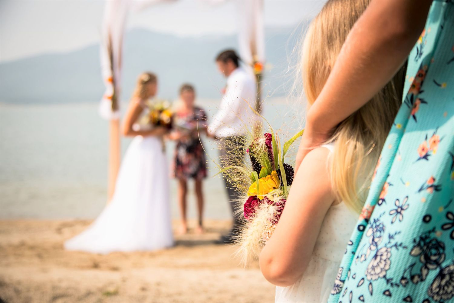 Wedding ceremony captured through guest's perspective with blurred flowers in foreground.