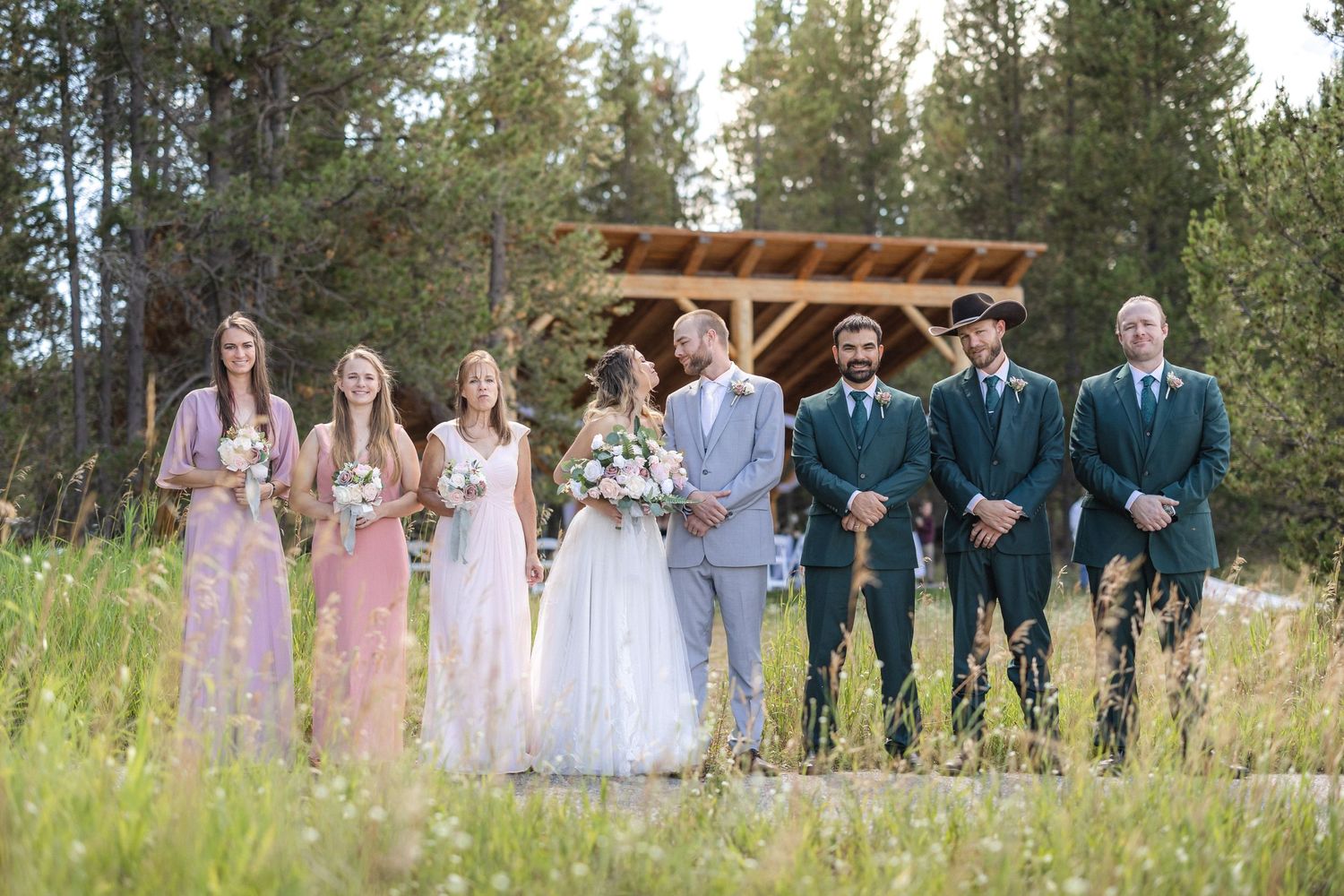 Wedding party members gathered in an outdoor setting with pine trees and a wooden pergola.