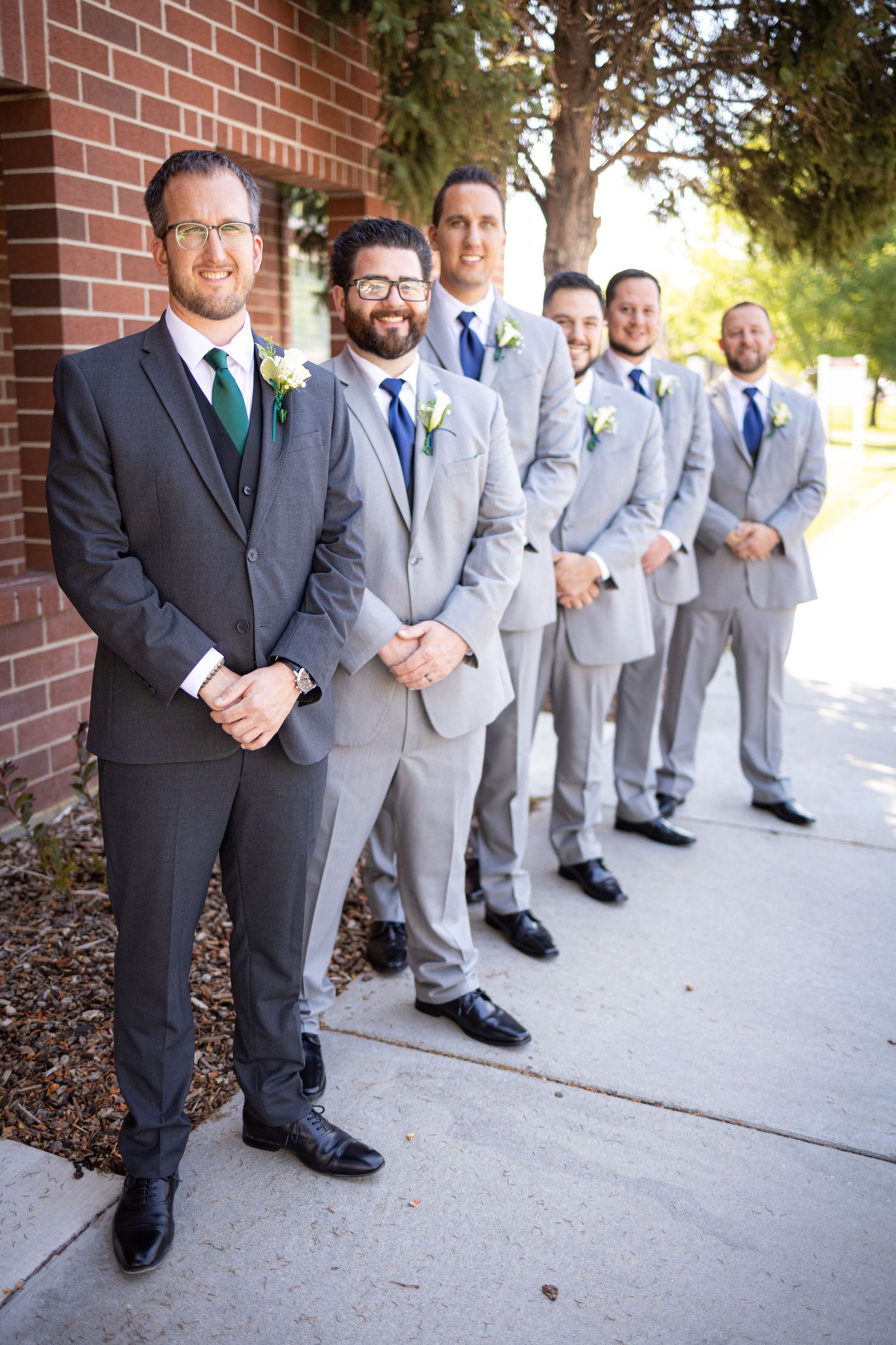 Groomsmen in suits line up against brick wall wearing matching boutonnieres.