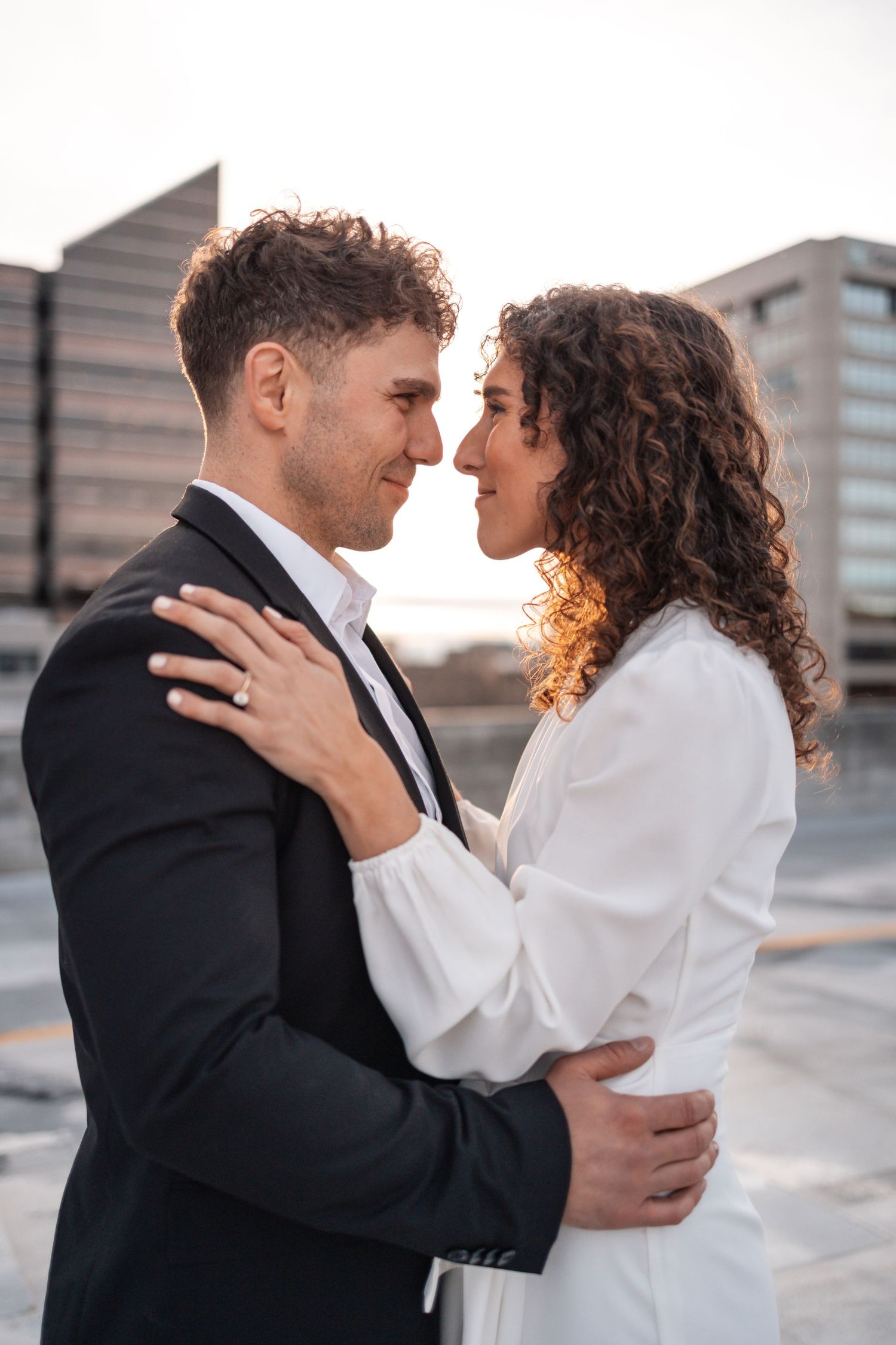 Tender moment between couple in formal attire on urban rooftop setting.