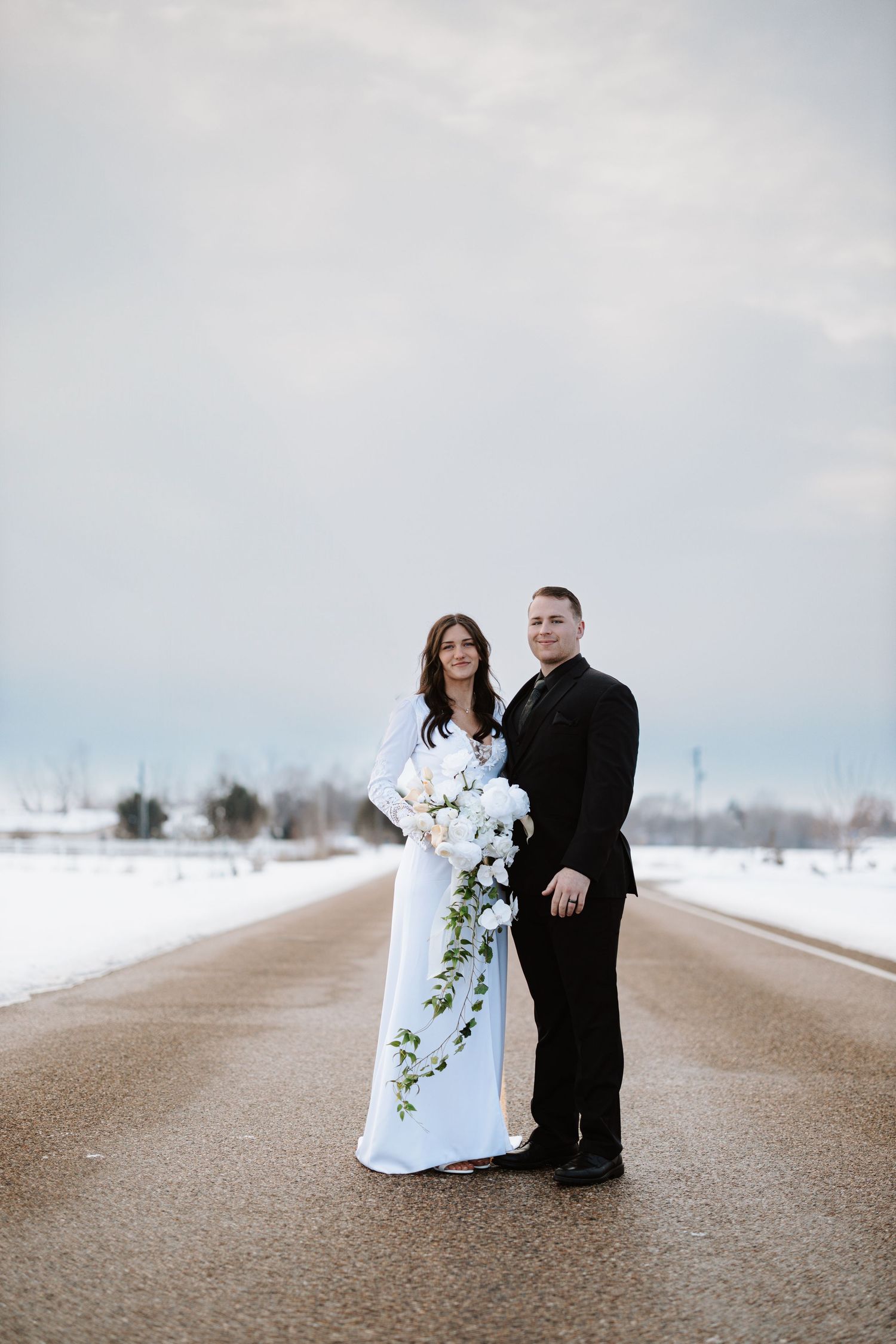 Elegant winter wedding portrait on snow-lined road with cascading bouquet.