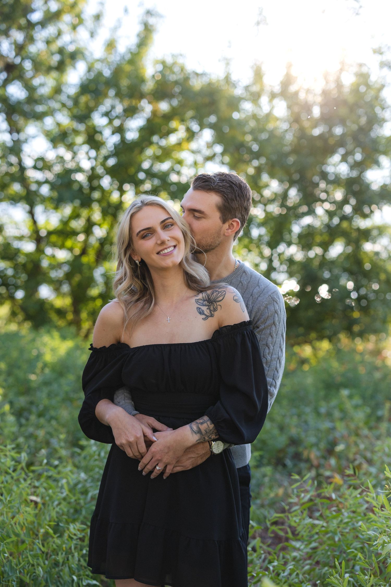 Sweet moment between couple in casual attire with golden sunlight filtering through trees.