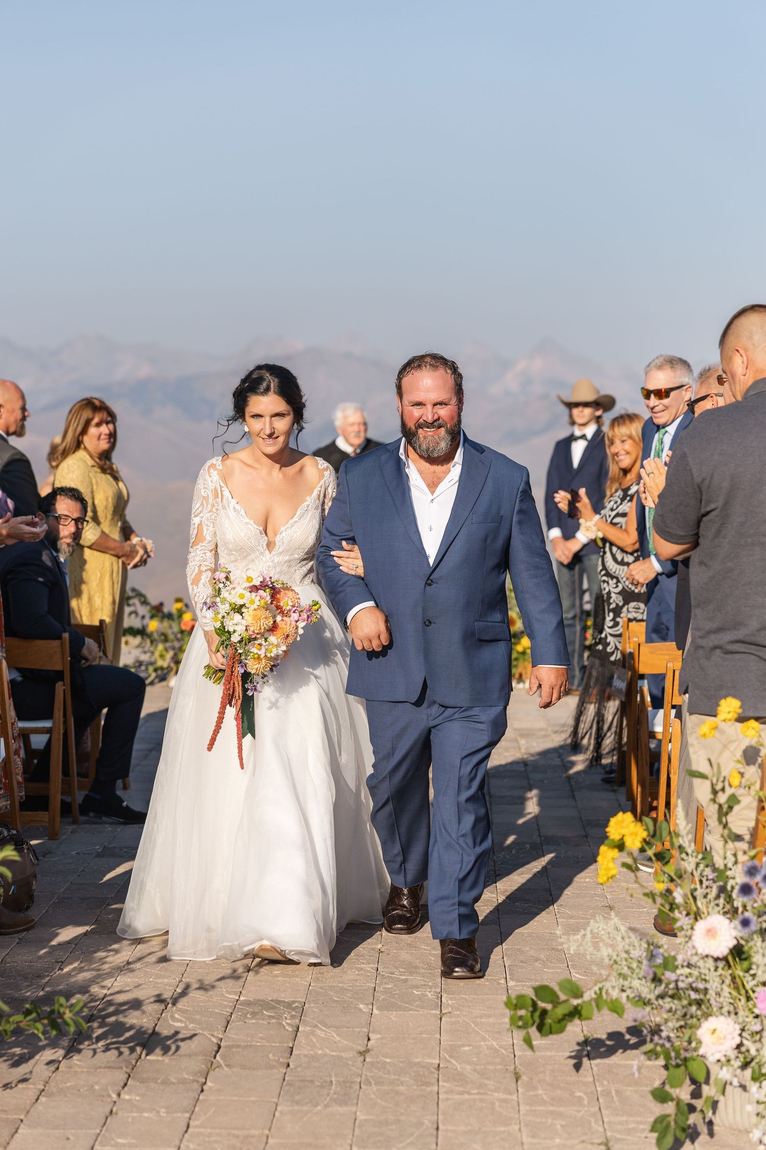 Wedding ceremony processional on a stone patio overlooking mountain landscapes.
