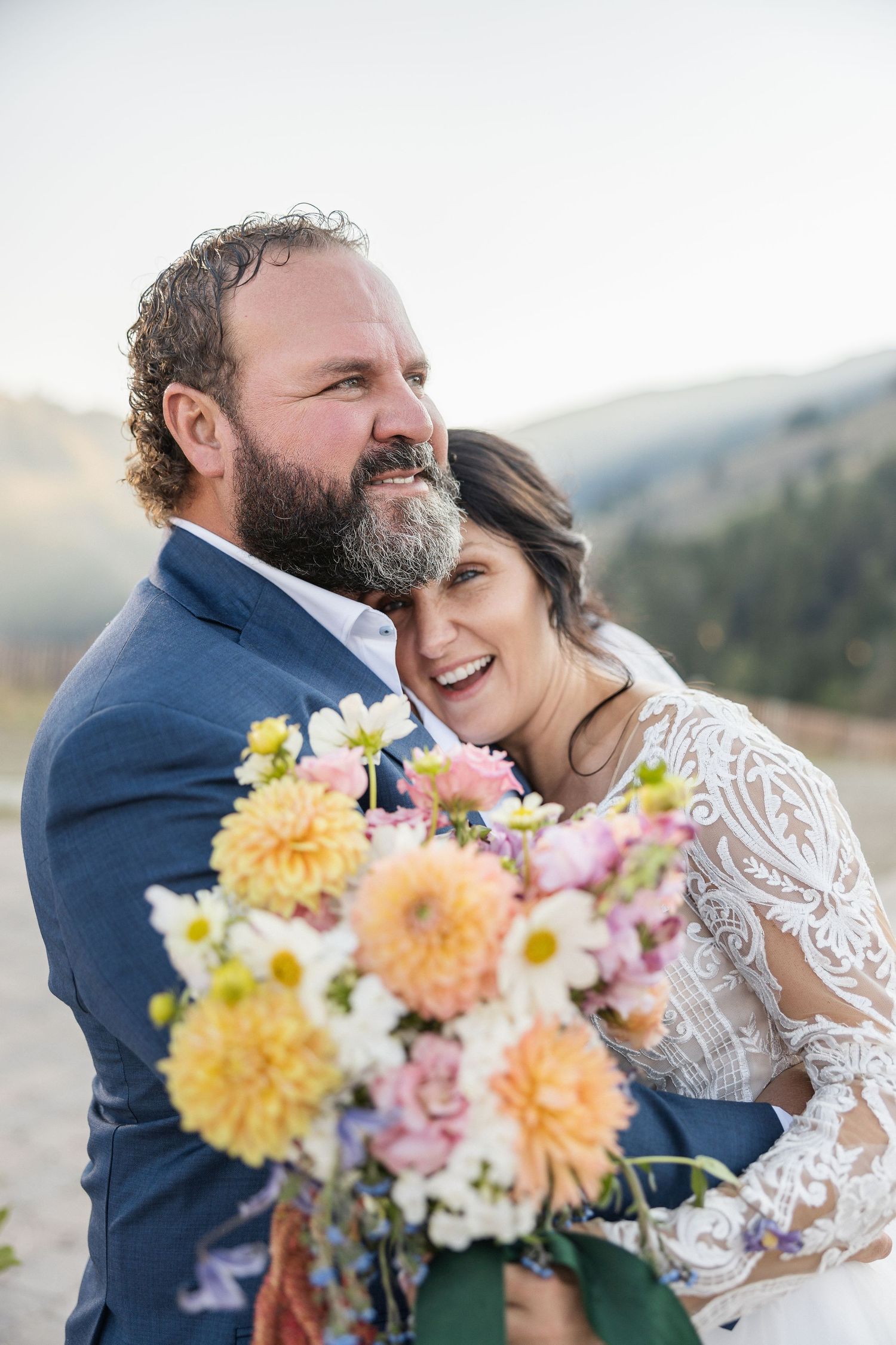 Colorful bridal bouquet with yellow and pink flowers against mountain backdrop.