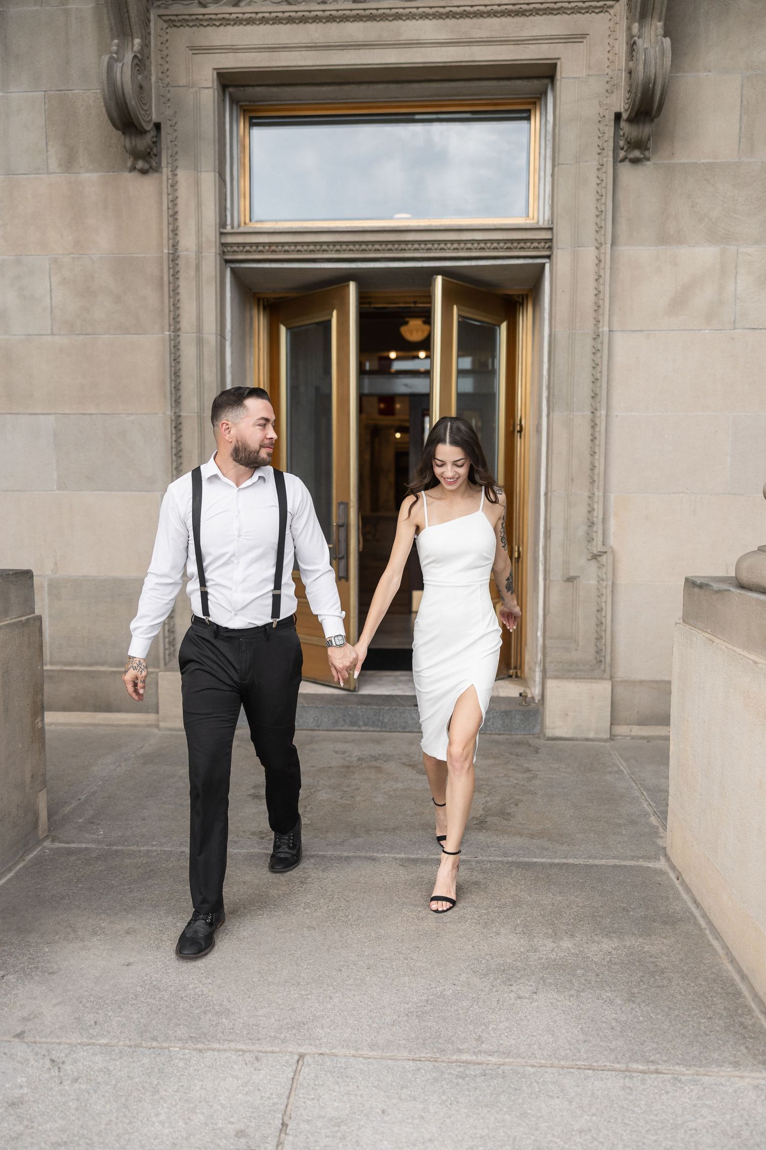 A couple walks together through an elegant doorway in formal attire.