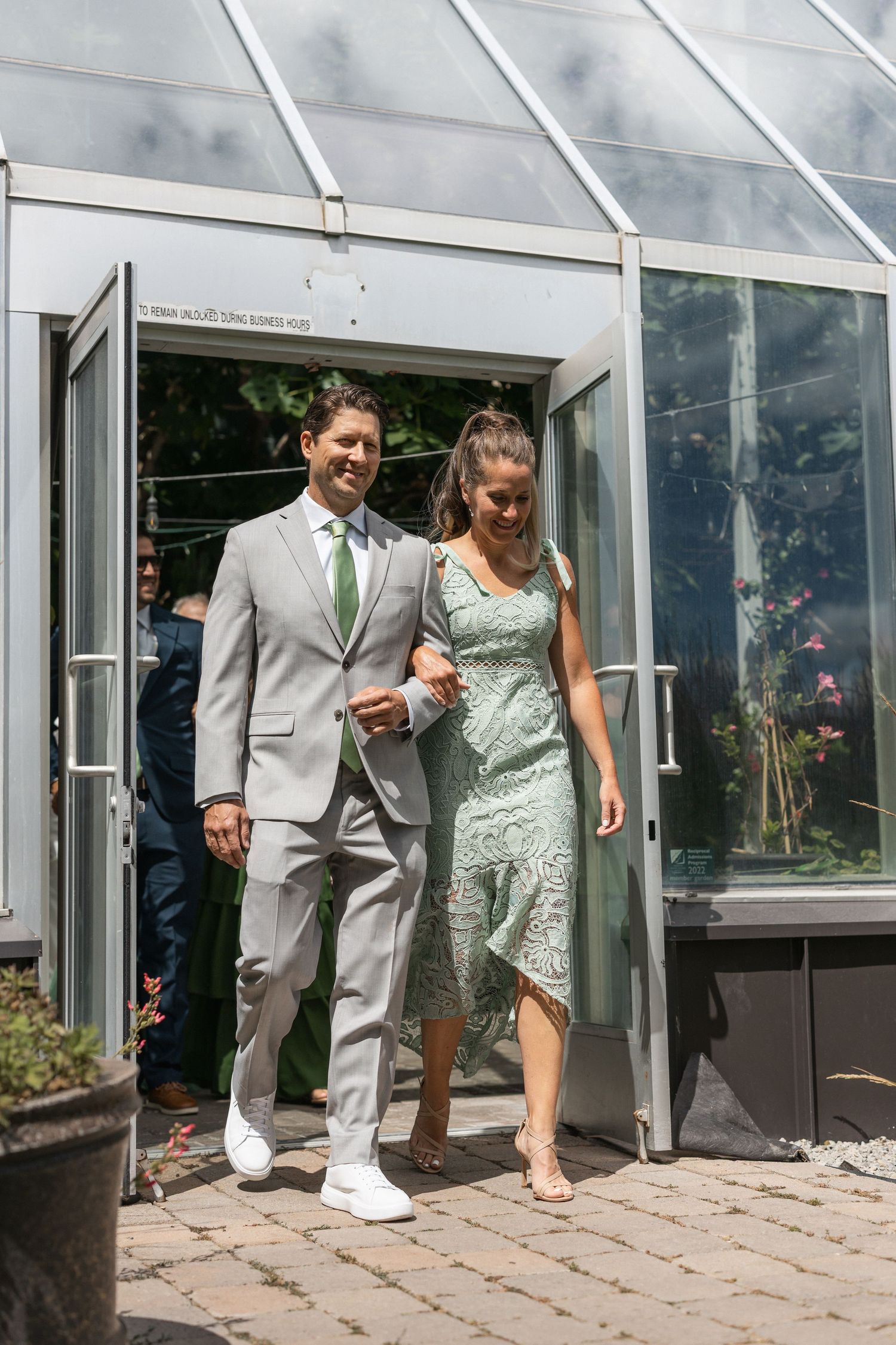 Wedding party exiting glass greenhouse during celebration.