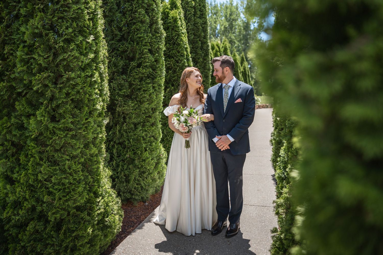 Couple walks together through garden pathway with green cypress trees.