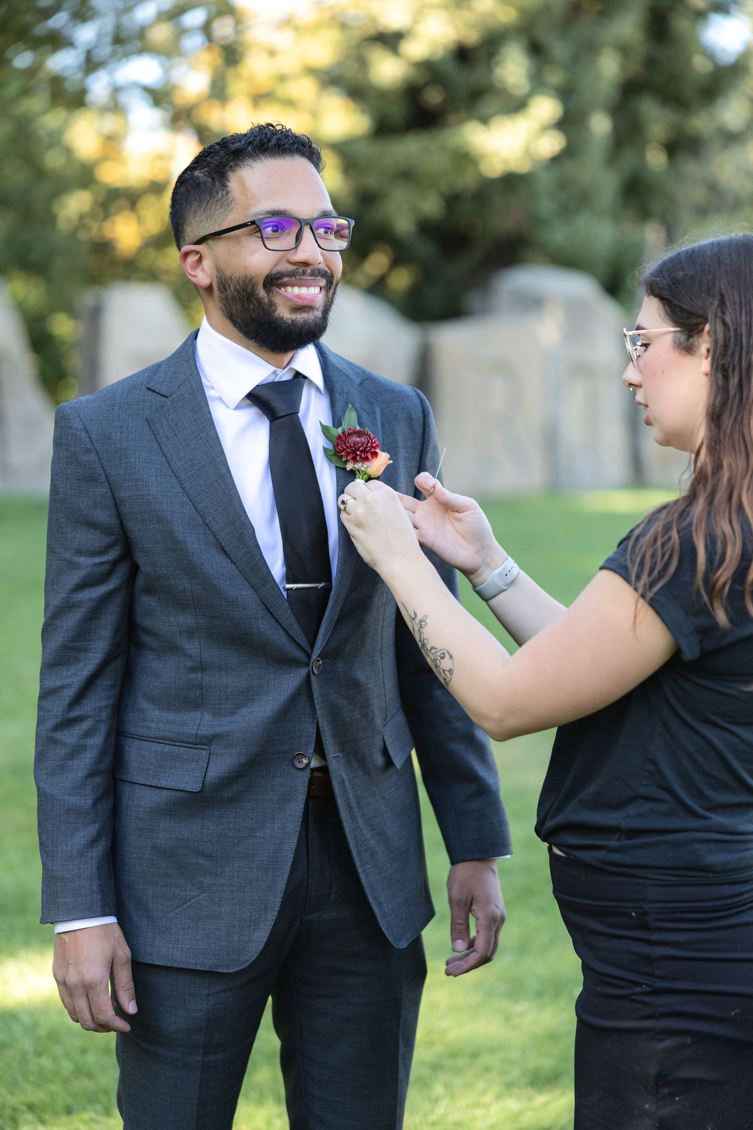 Wedding party members help pin boutonnieres onto suits during an outdoor ceremony.