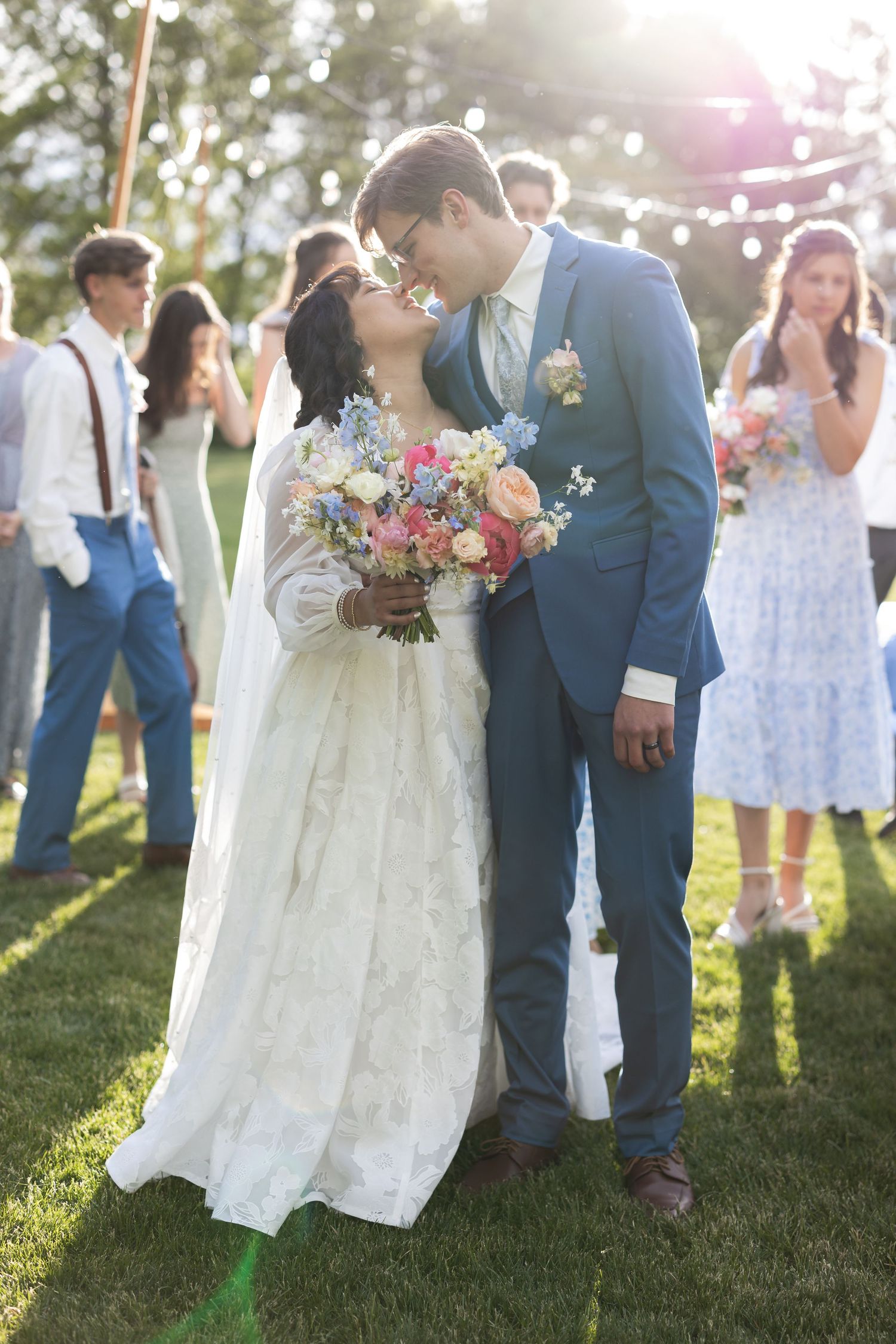 A newlywed couple shares a romantic moment under string lights at their outdoor wedding ceremony.