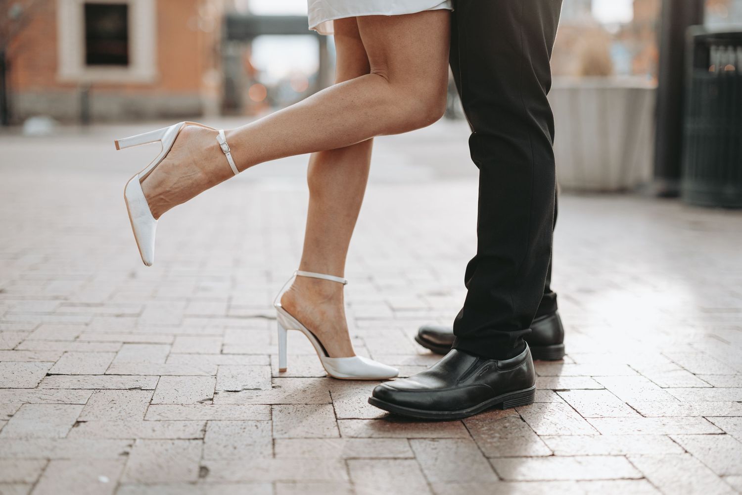 Close-up of formal shoes and legs with woman in heels and man in dress shoes on brick pavement.