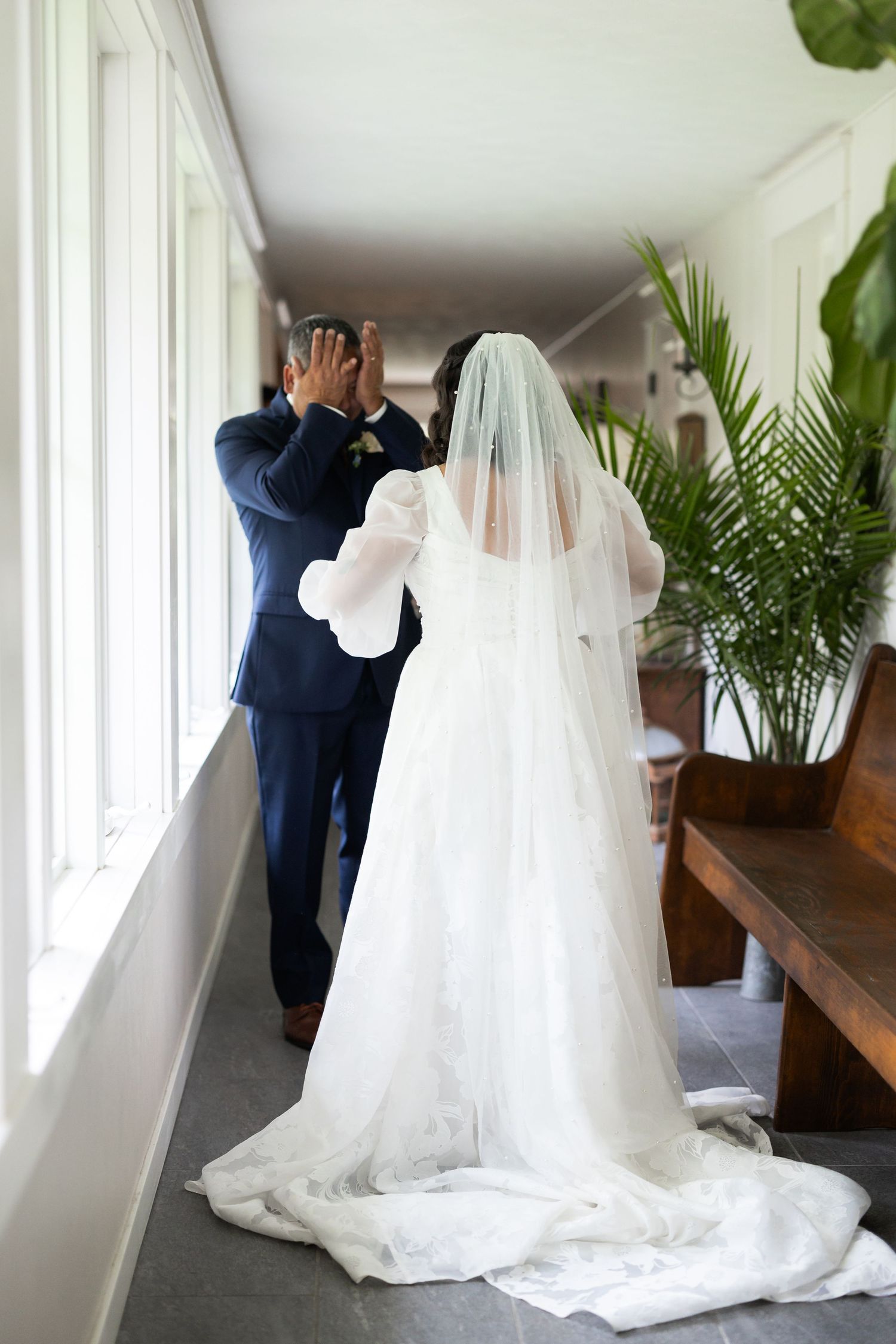 First look wedding moment in bright hallway with trailing white gown.