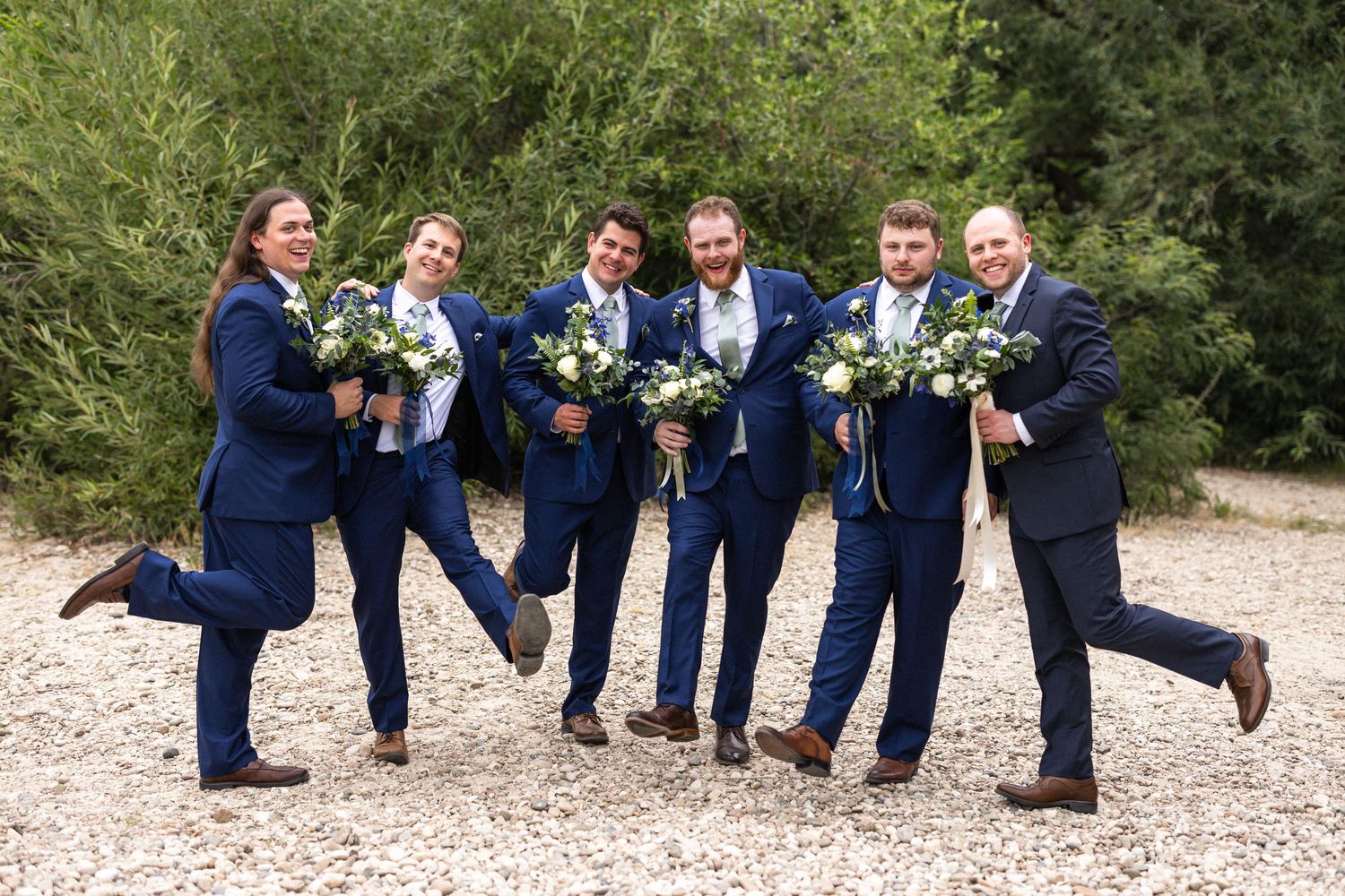 Groomsmen strike playful pose holding bouquets while wearing navy suits.