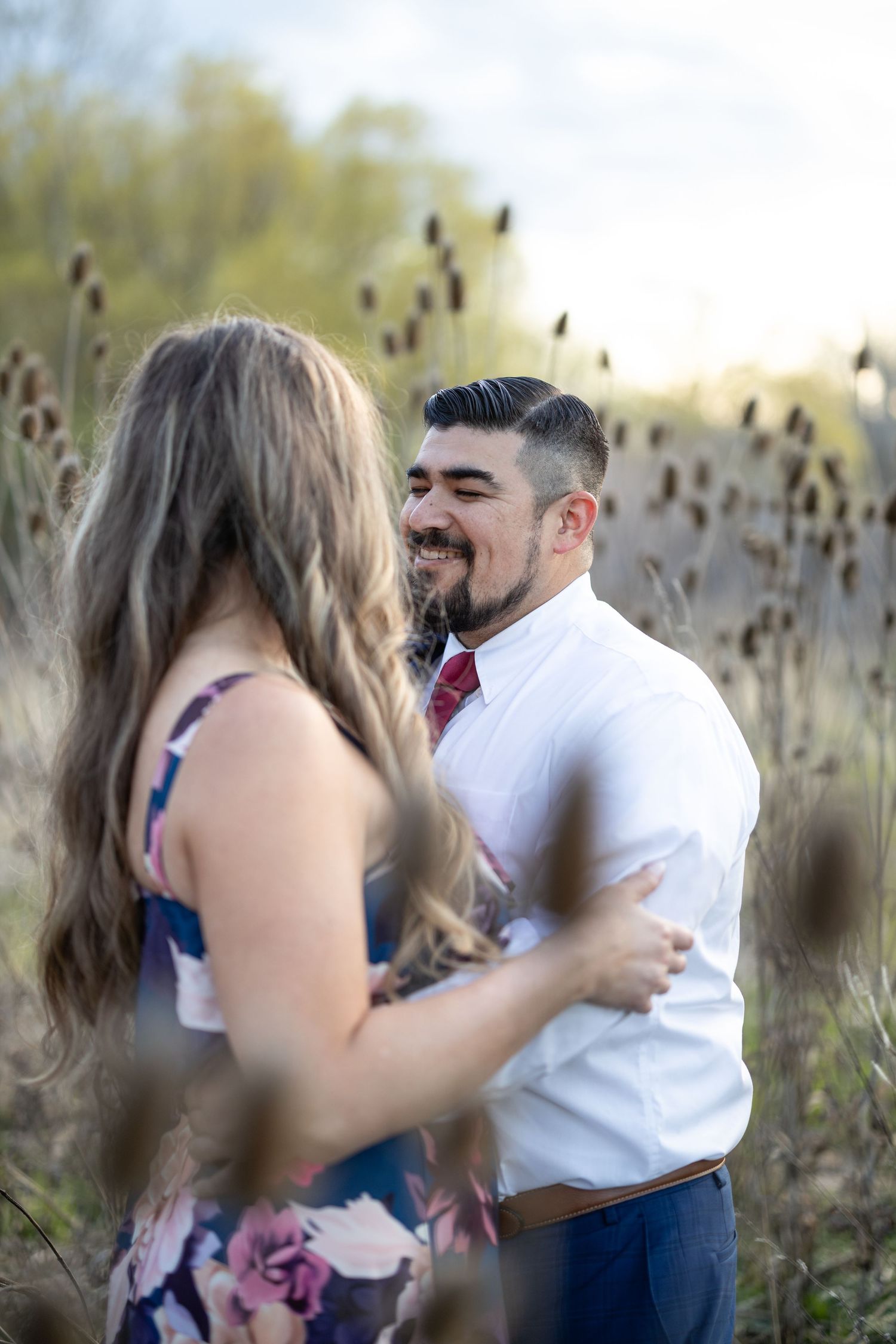Joyful moment captured between couple in formal attire surrounded by dried cattails.