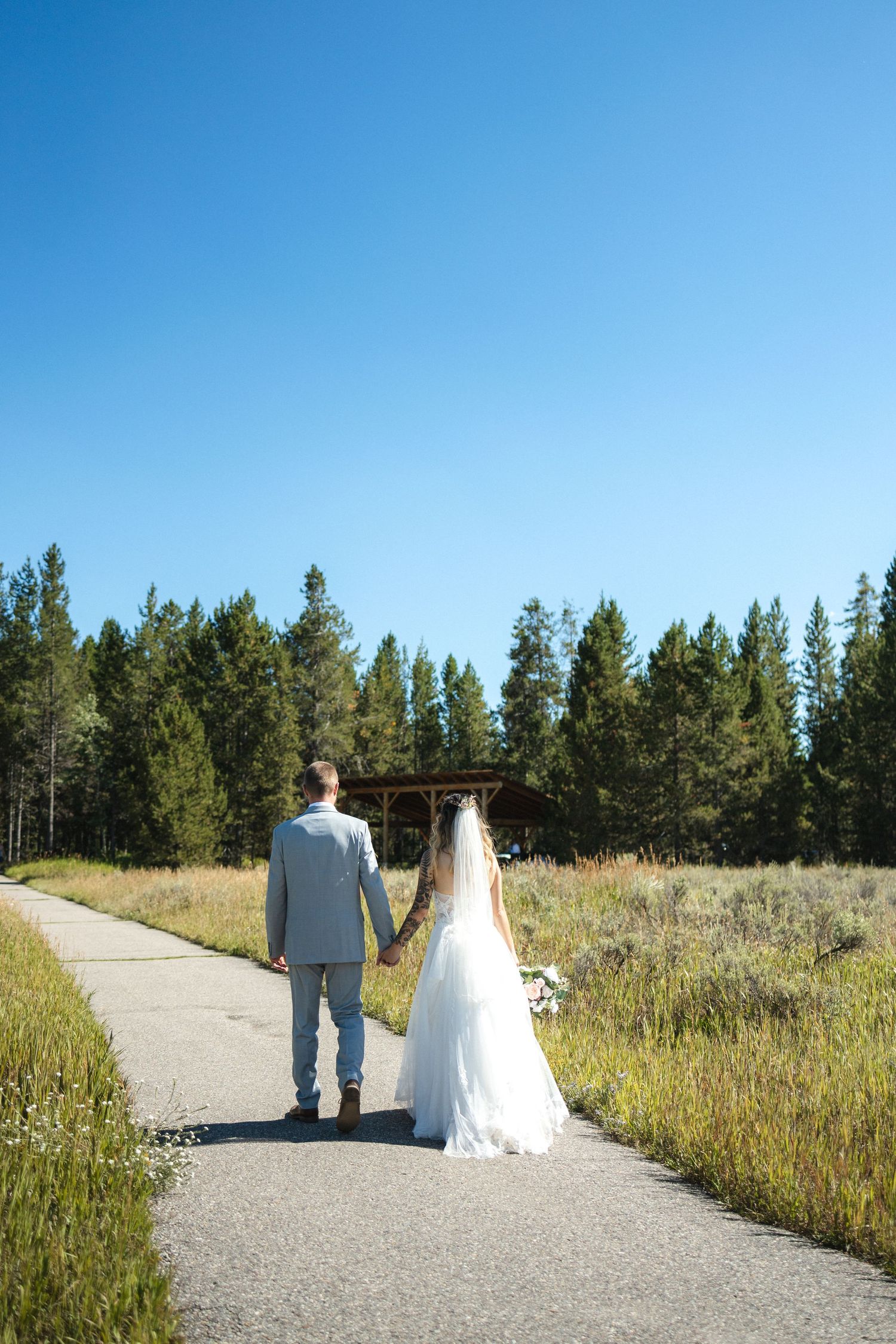 A couple walks hand in hand down a path through golden mountain meadows.