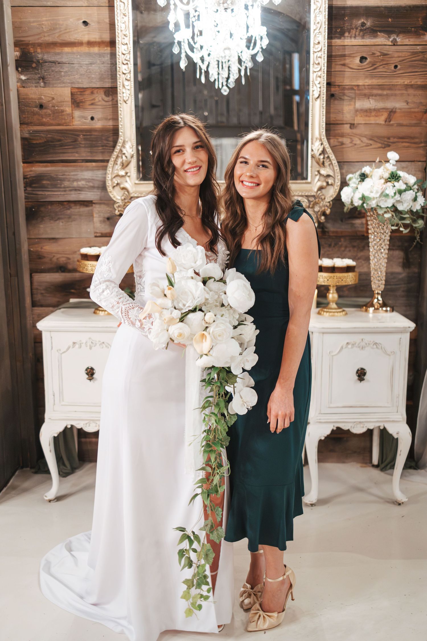 Wedding scene with ornate mirror, white dresser and crystal chandelier in rustic wooden setting.