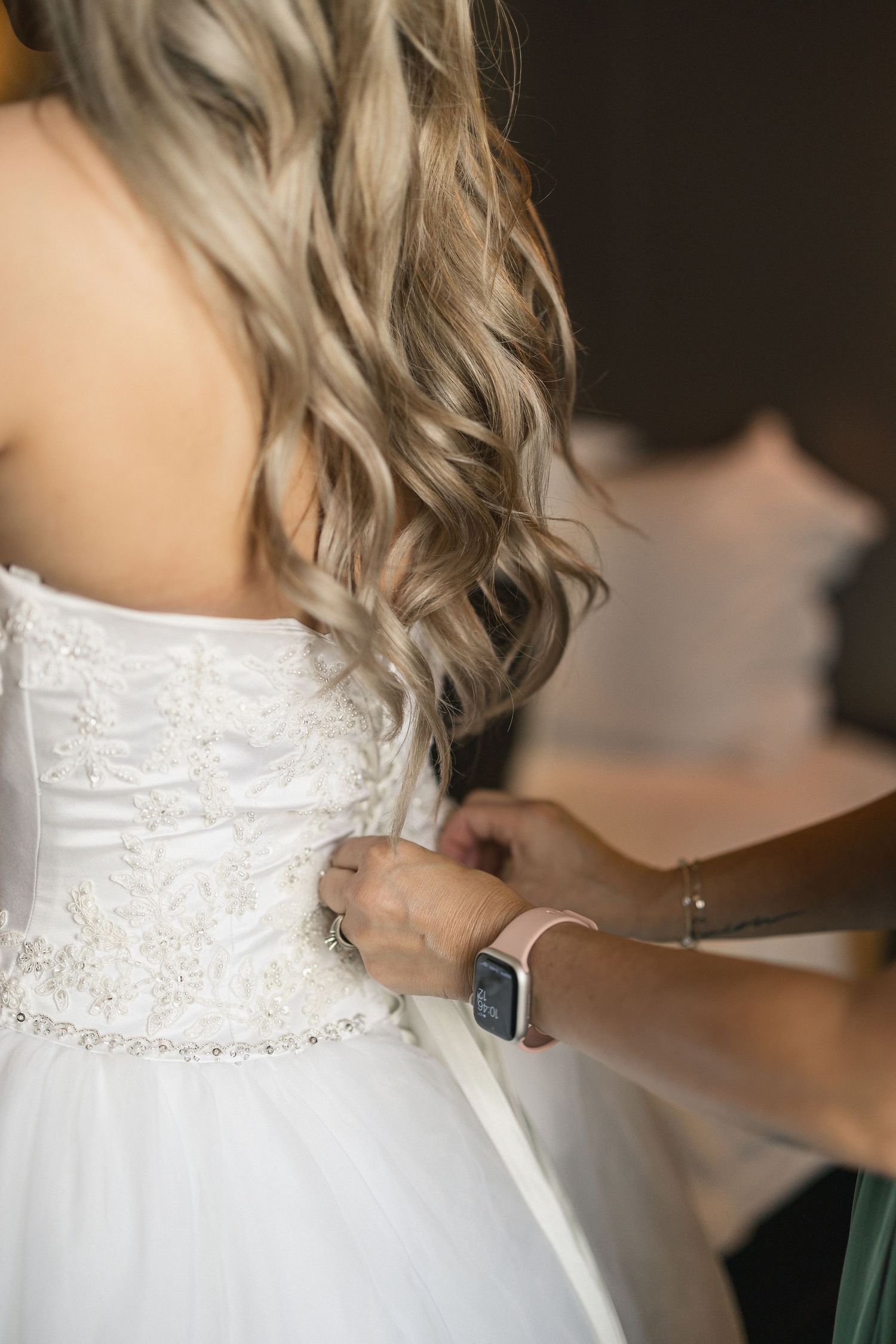 Close-up of hands lacing up intricate white beaded wedding dress.