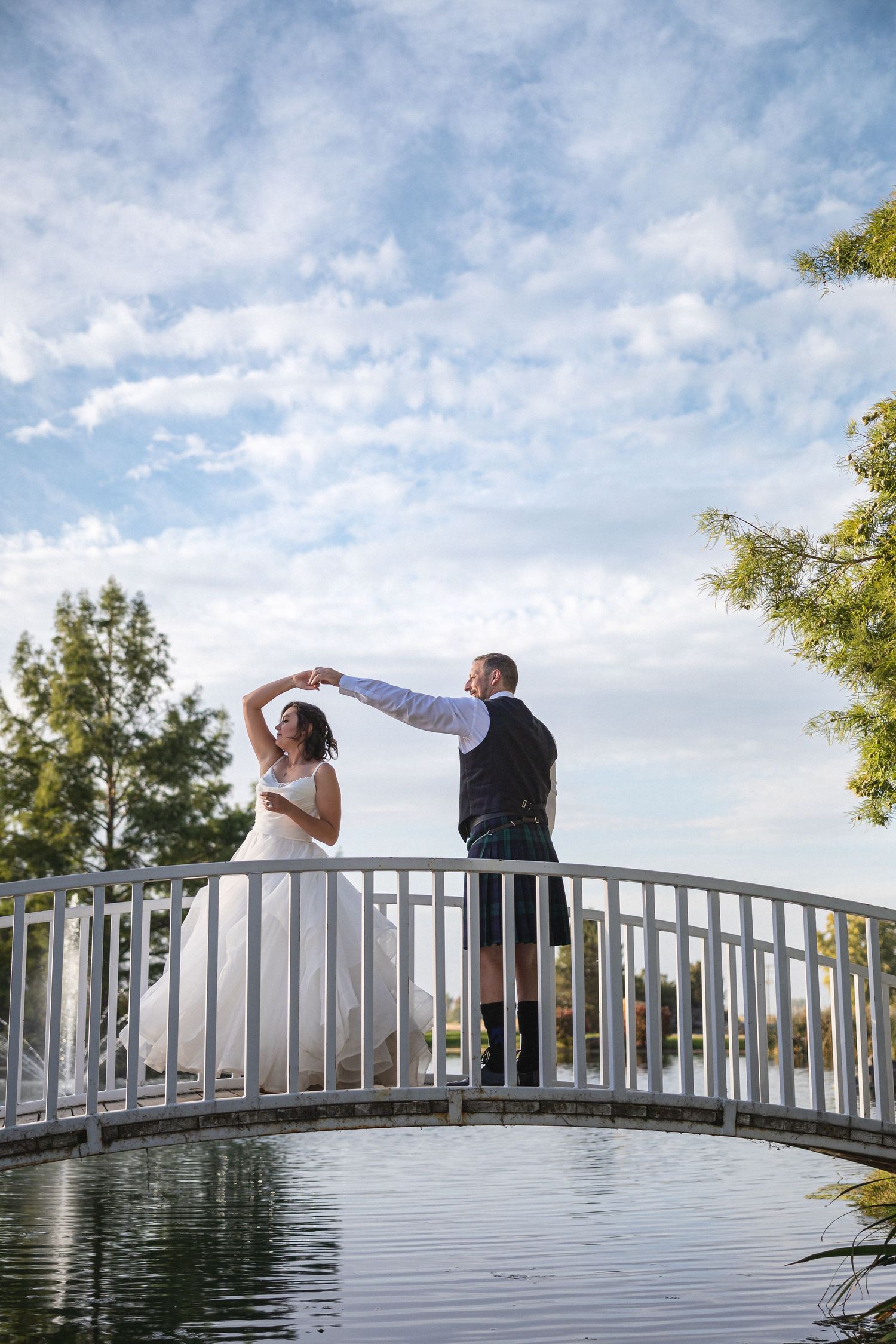 A couple shares a playful dancing moment on a white bridge during their wedding.