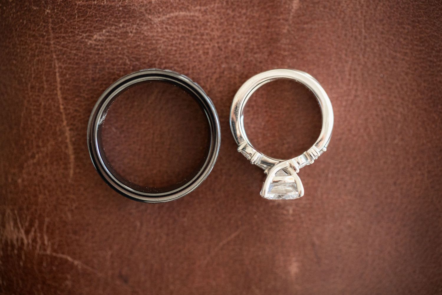 Wedding rings photographed on a brown leather surface, featuring a diamond engagement ring.