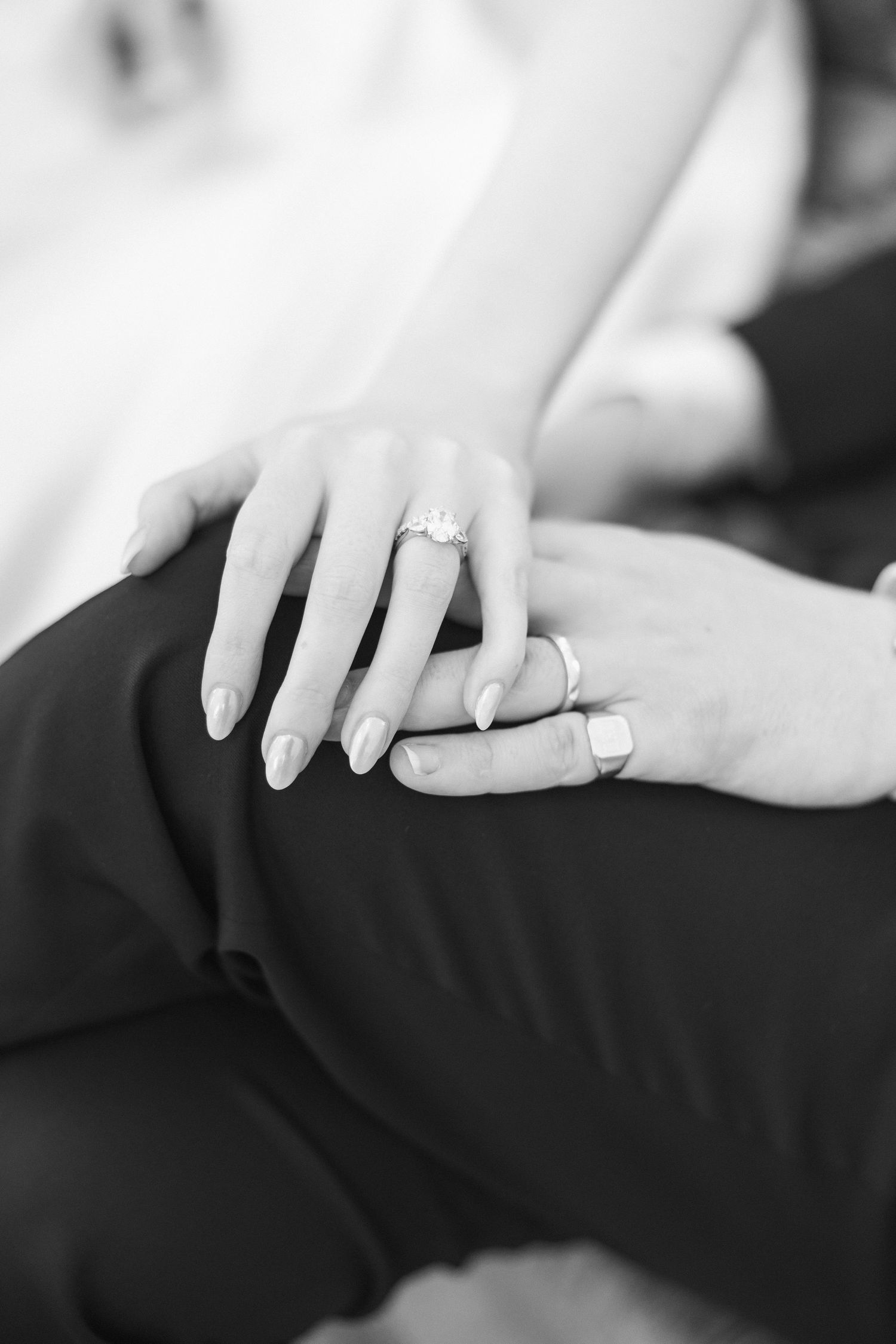 Close-up black and white photo of hands with engagement and wedding rings.