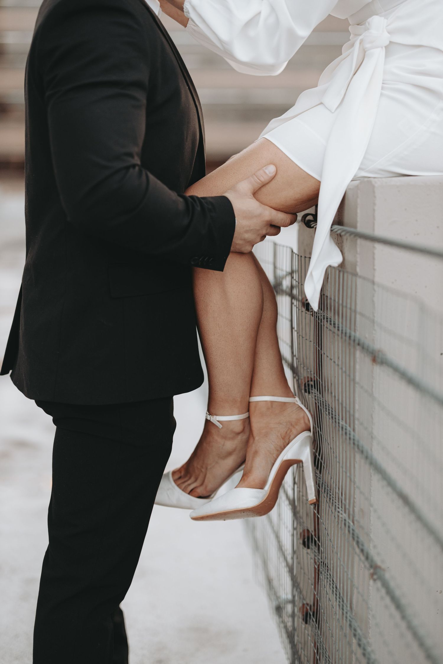 Close-up shot of a couple's intimate moment against a wall, focusing on white heels and formal attire.