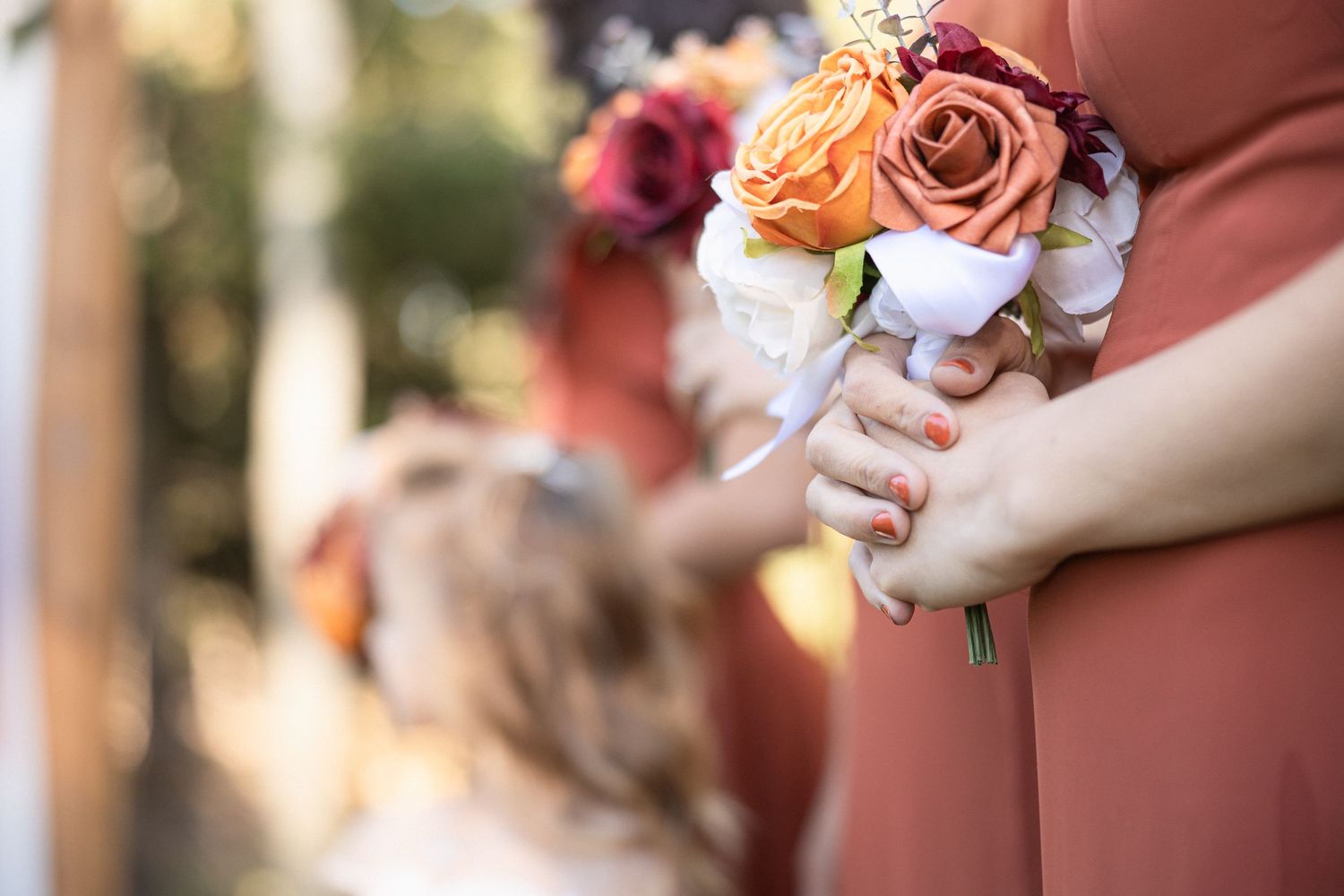Close-up of peach and burgundy rose bouquet being held against coral colored fabric.