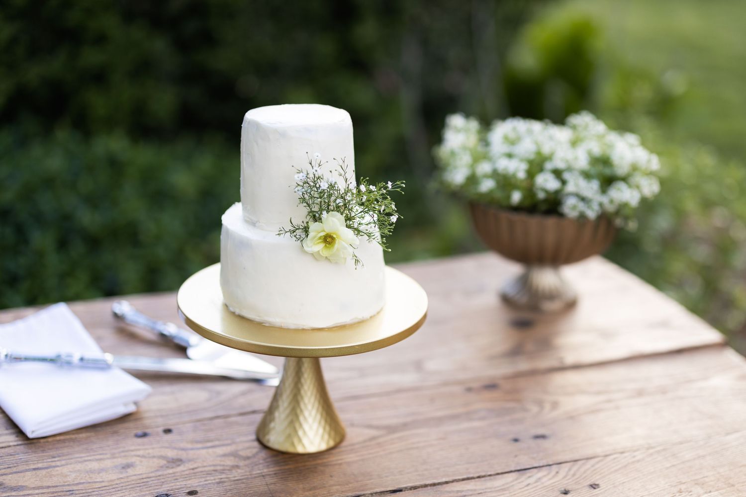 Simple two-tier white wedding cake decorated with delicate flowers on gold stand.